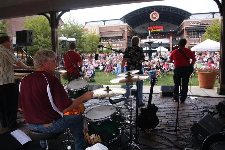 Live band performing on stage with audience outdoors at a concert venue.