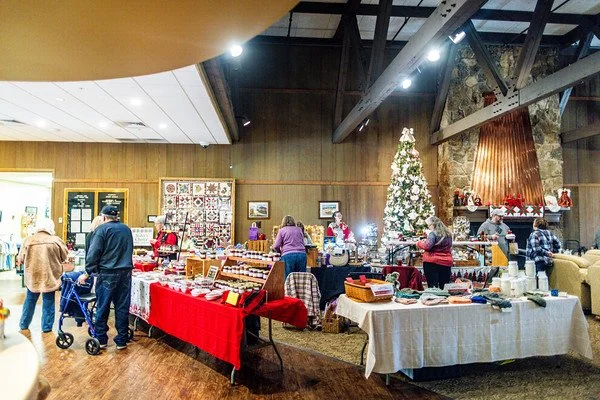 Indoor holiday craft fair with Christmas tree, vendors, and shoppers.