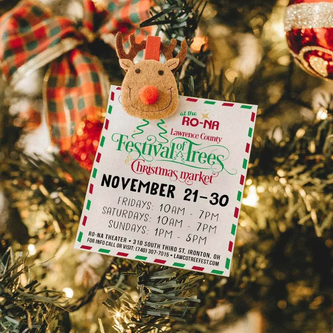 A festive ornament on a Christmas tree featuring a felt reindeer head with a red nose and antlers. Attached to the tree is a flyer for the Lawrence County Festival of Trees and Christmas Market, detailing event dates and times from November 21 to 30.