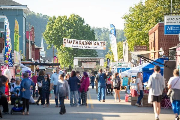 Crowd walking down Main Street at Greentop's Fall Festival with booths and tents on both sides, and a large banner overhead reading 'Old Fashion Days'.