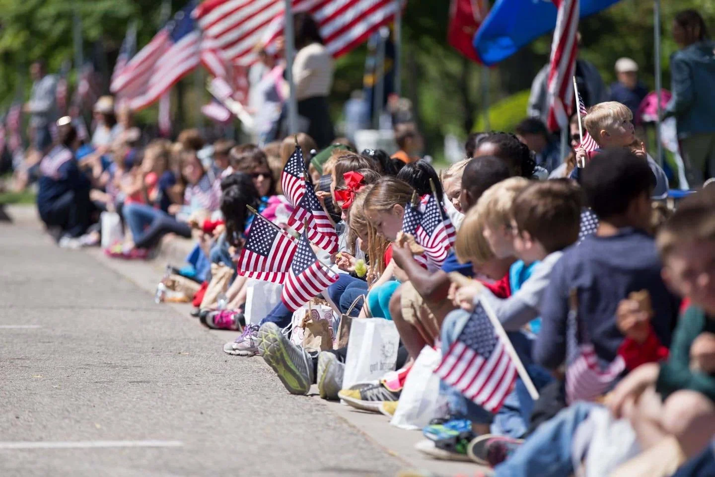 Kids sitting on the curb holding small American flags during a patriotic event.
