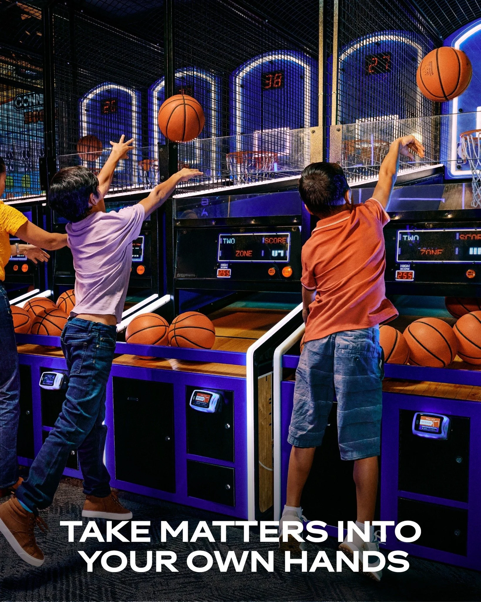 Children playing arcade basketball game at an indoor amusement center, shooting basketballs into hoops.
