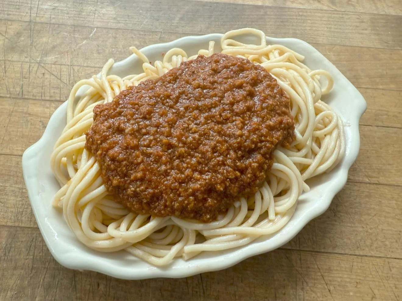 Plate of cooked spaghetti topped with meat sauce on a wooden surface.