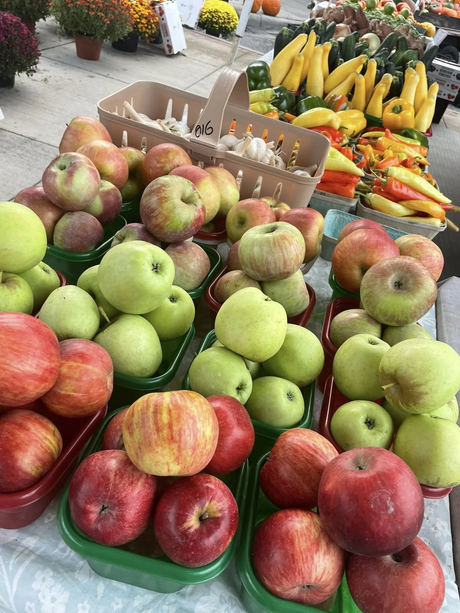 Display of various apples and colorful peppers at an outdoor market.