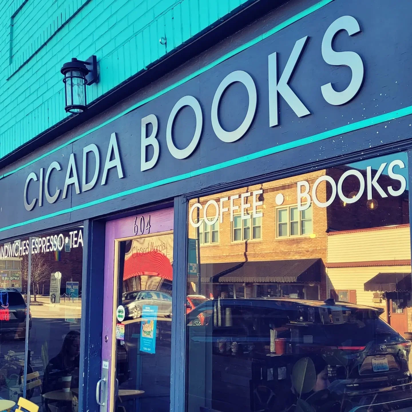 Exterior view of Cicada Books storefront with large sign, windows reflecting street scene, and door with purple frame