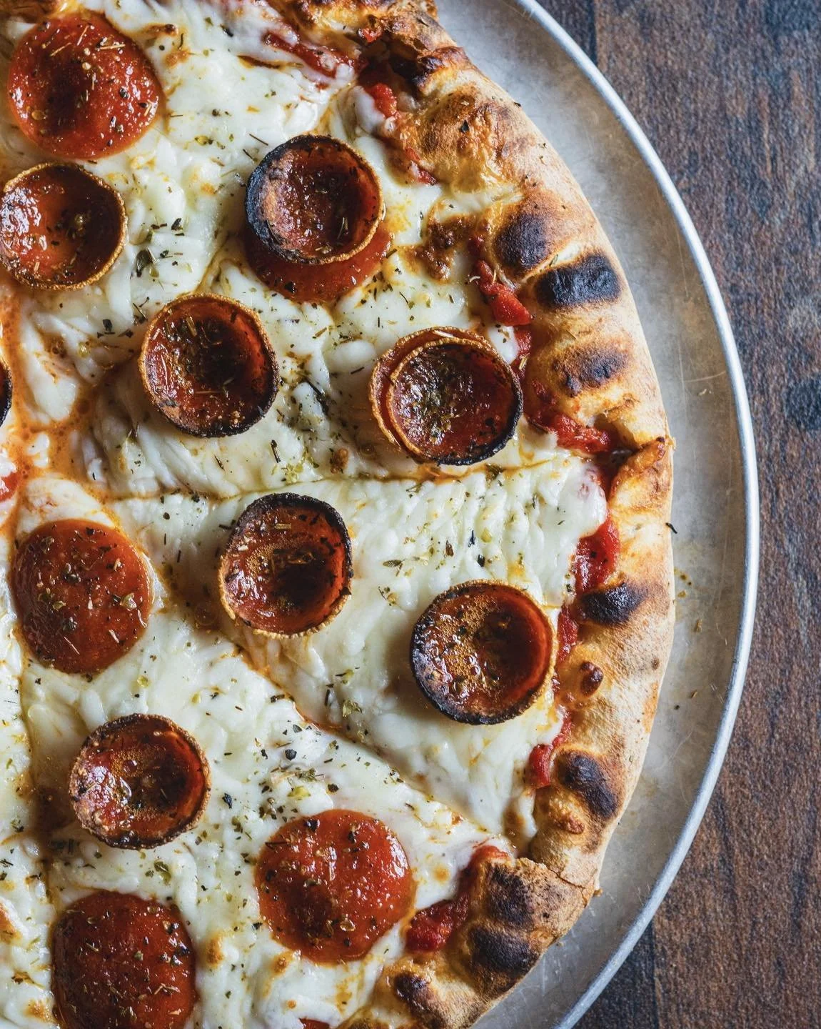 Pizza with pepperoni slices and melted cheese on a crust, served on a metal tray.
