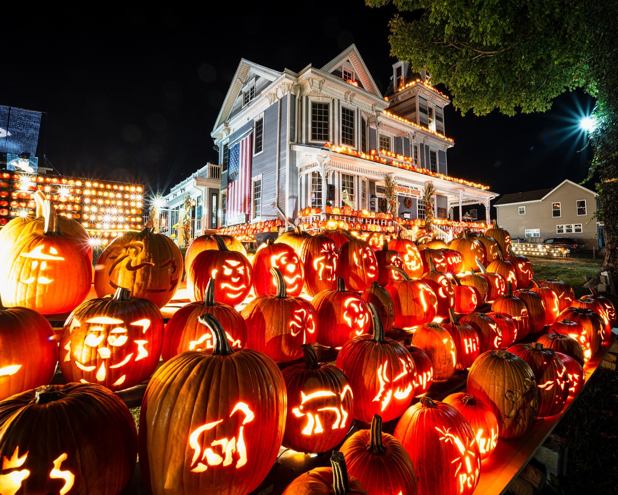 Decorated house and porch with many carved, lit pumpkins for Halloween at night.