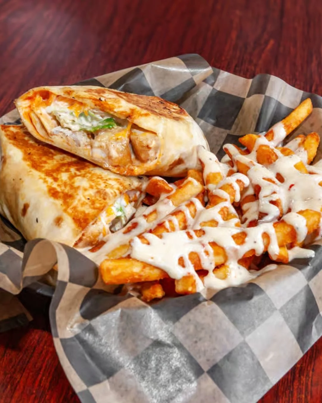 Grilled chicken wrap and seasoned French fries topped with white cheese sauce on checkered paper