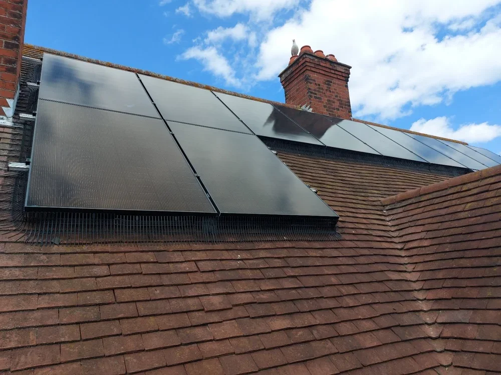 Solar panels installed on a rooftop with a brick chimney in the background and a blue sky with clouds.