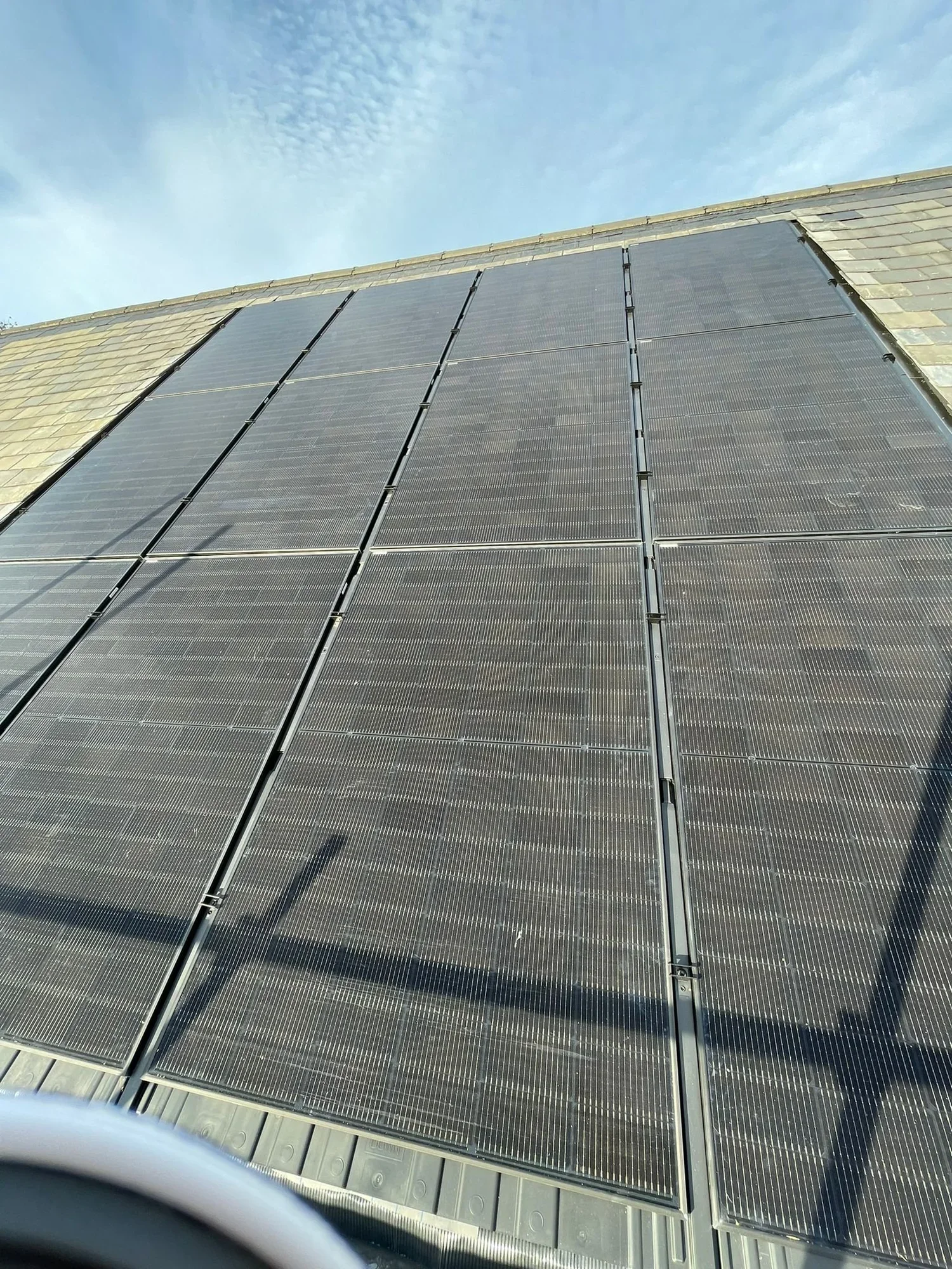A building's exterior wall covered with solar panels under a blue sky with some clouds.