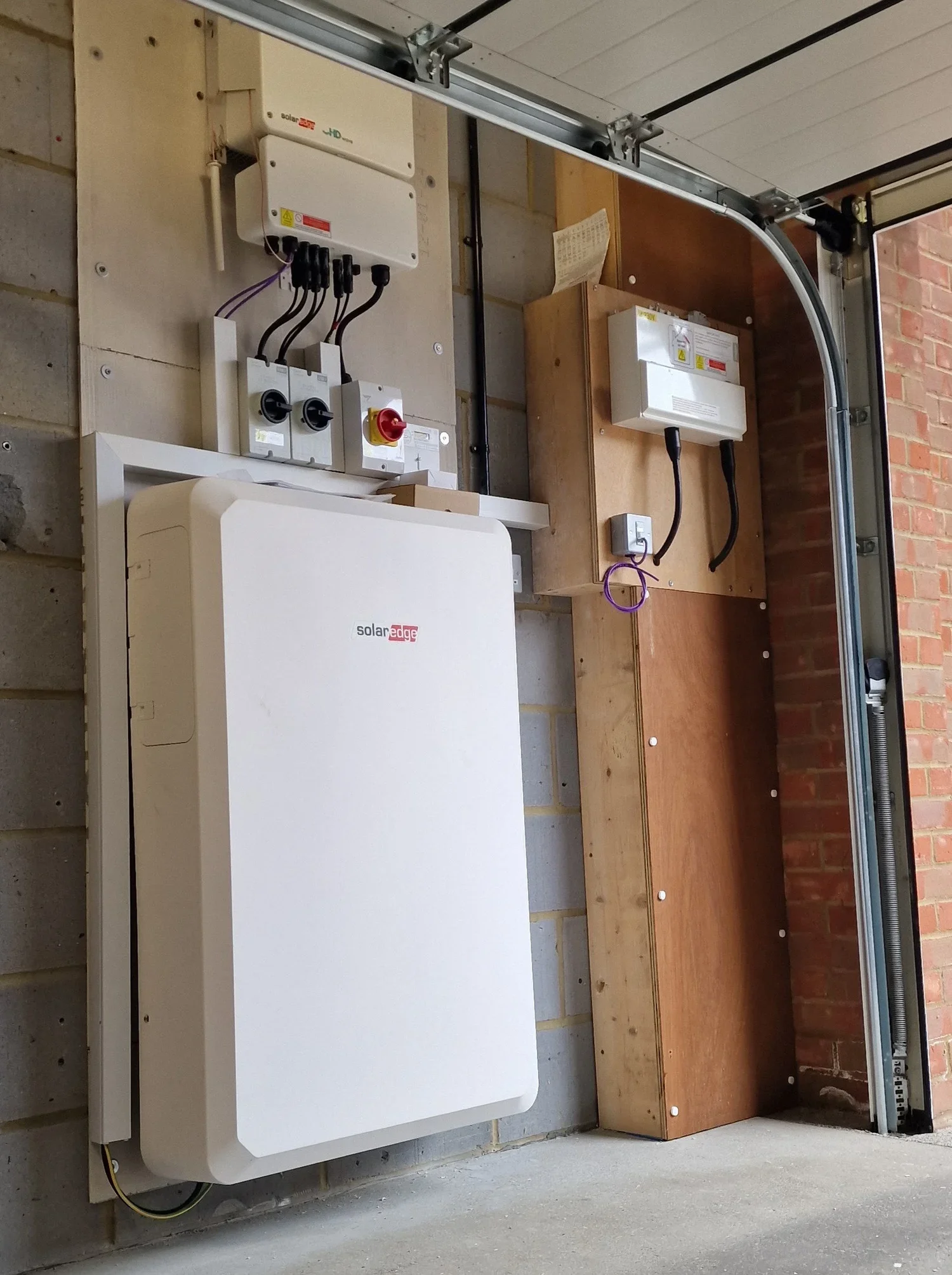Electrical equipment and solar inverter mounted on a garage wall, with wires and control boxes visible.
