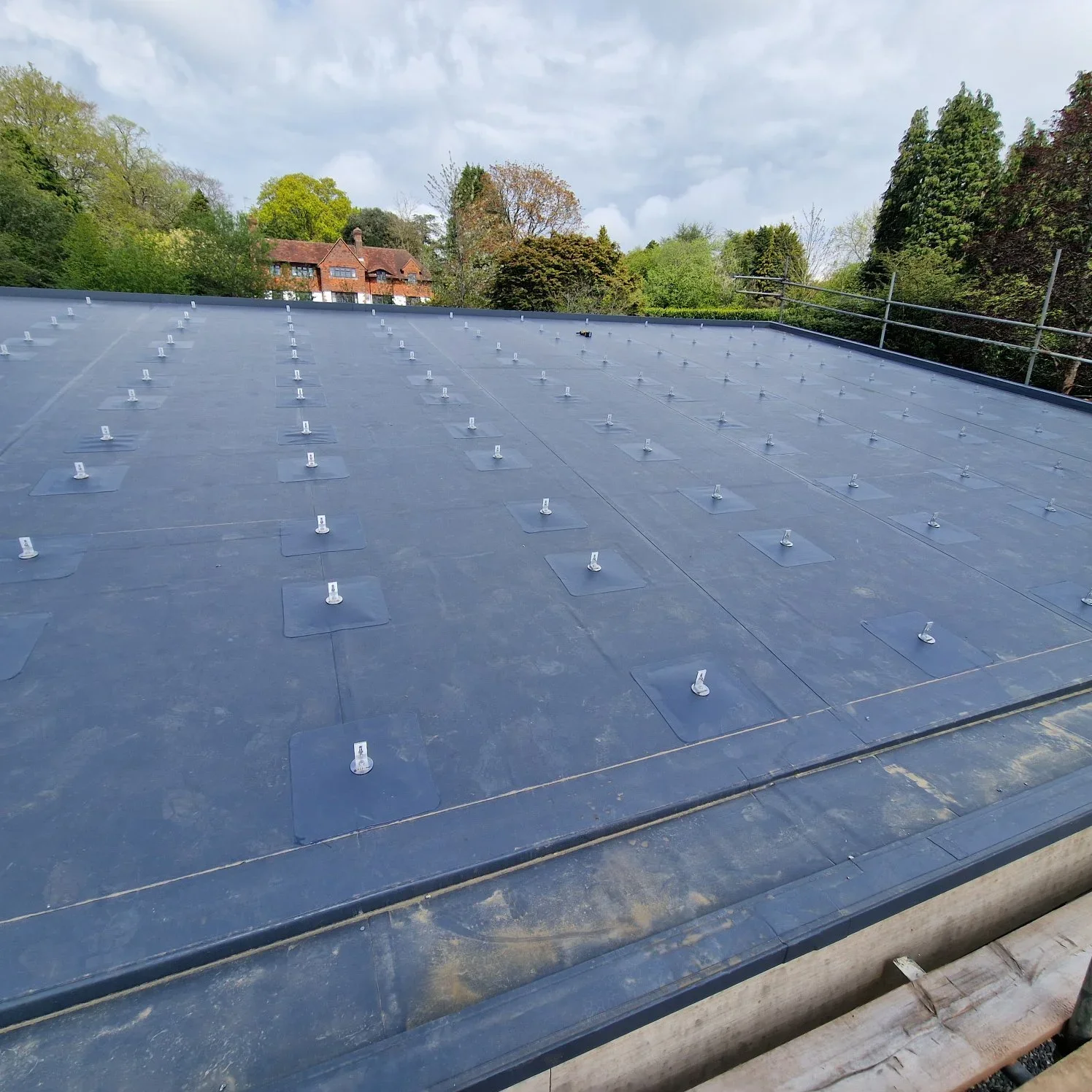 Roof with solar panel mounting brackets installed, surrounded by trees and buildings in the background.