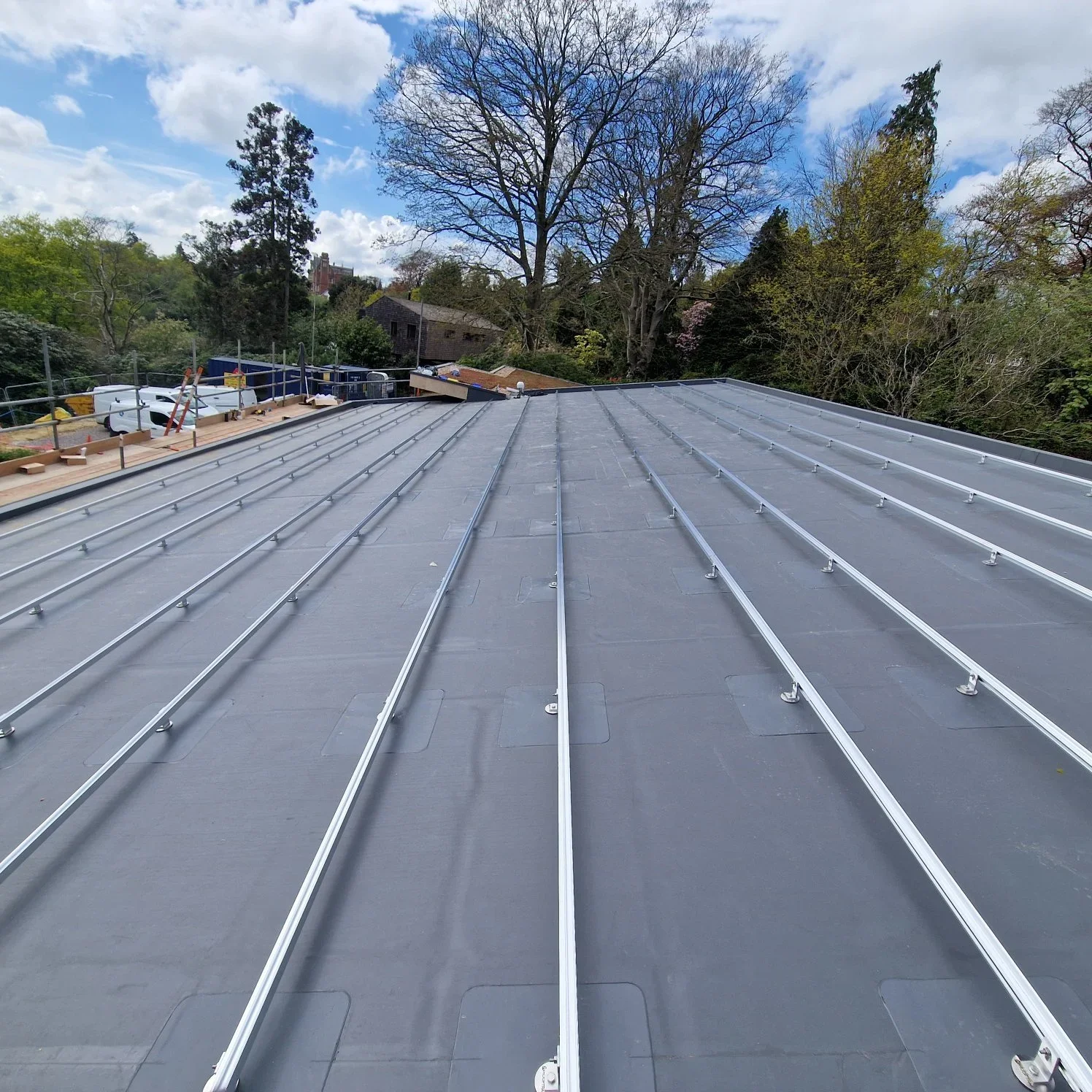 A metal roof under construction on a building, with trees and a partly cloudy sky in the background.