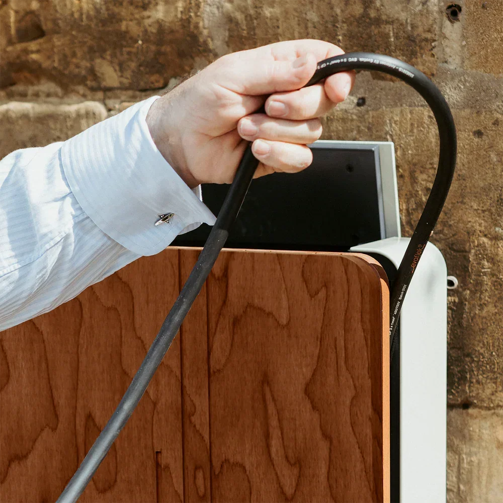 A person in a white dress shirt plugging in a power cable into an electronic device on a wooden desk.