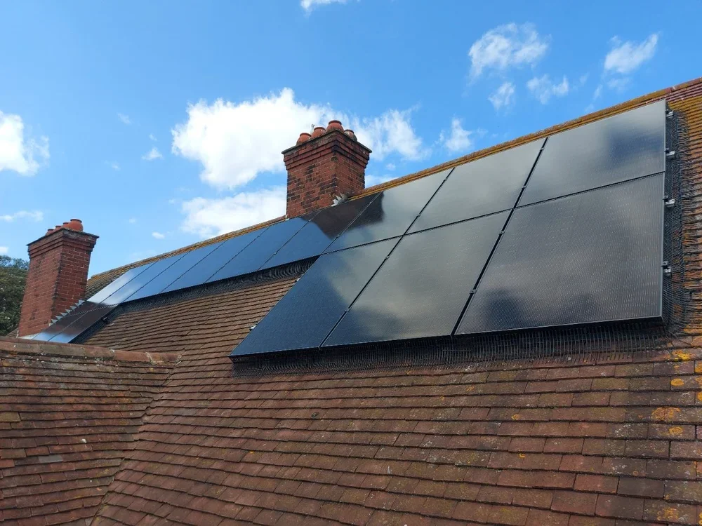 Solar panels installed on a sloped brick roof under a partly cloudy sky.