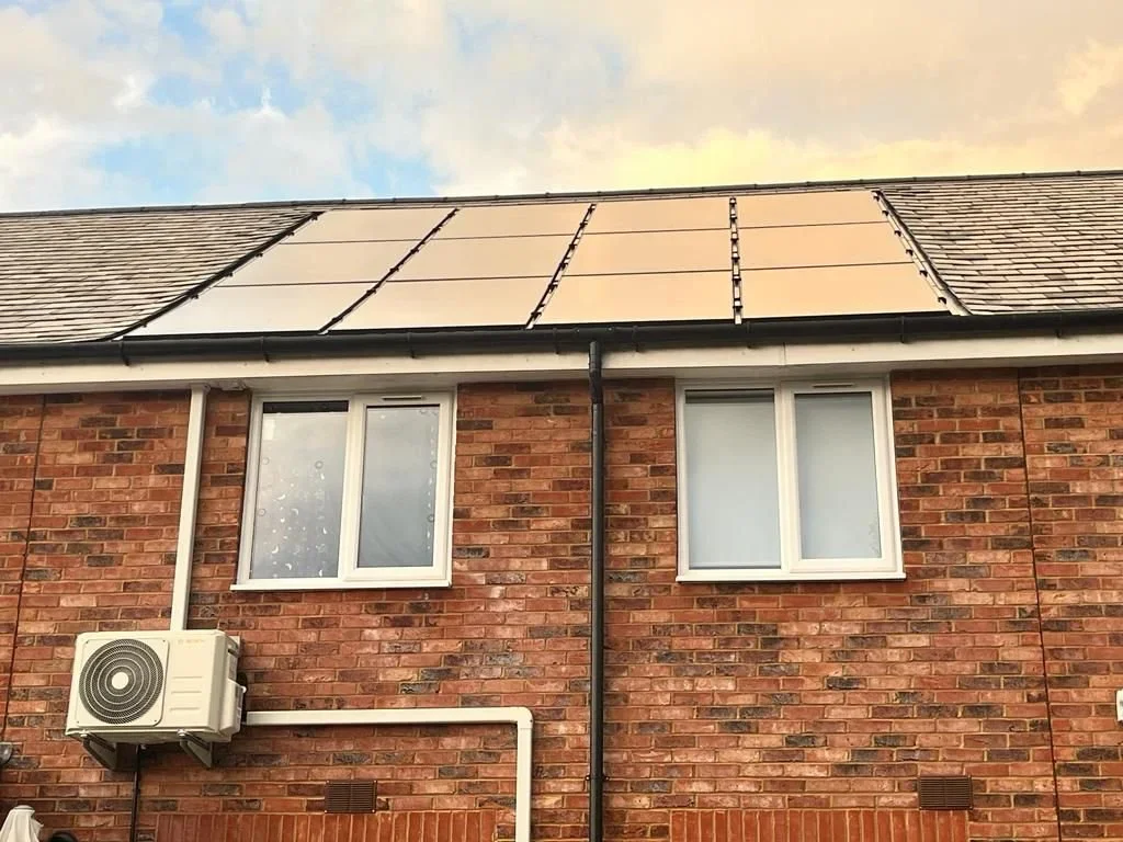 The roof of a brick house with solar panels installed, two white-framed windows, and an external air conditioning unit.