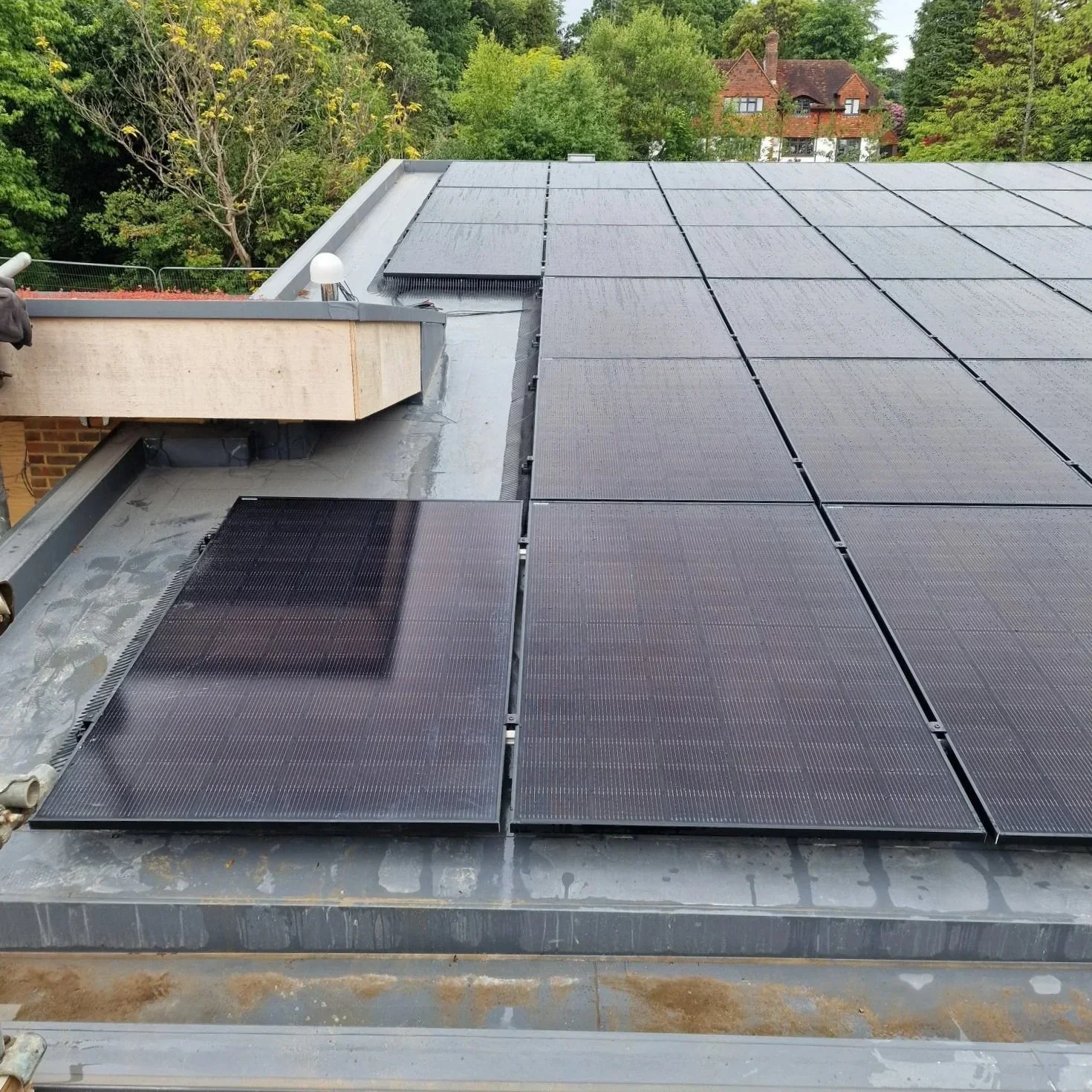 On a roof, installed solar panels with a backdrop of green trees and rooftops of neighboring houses.