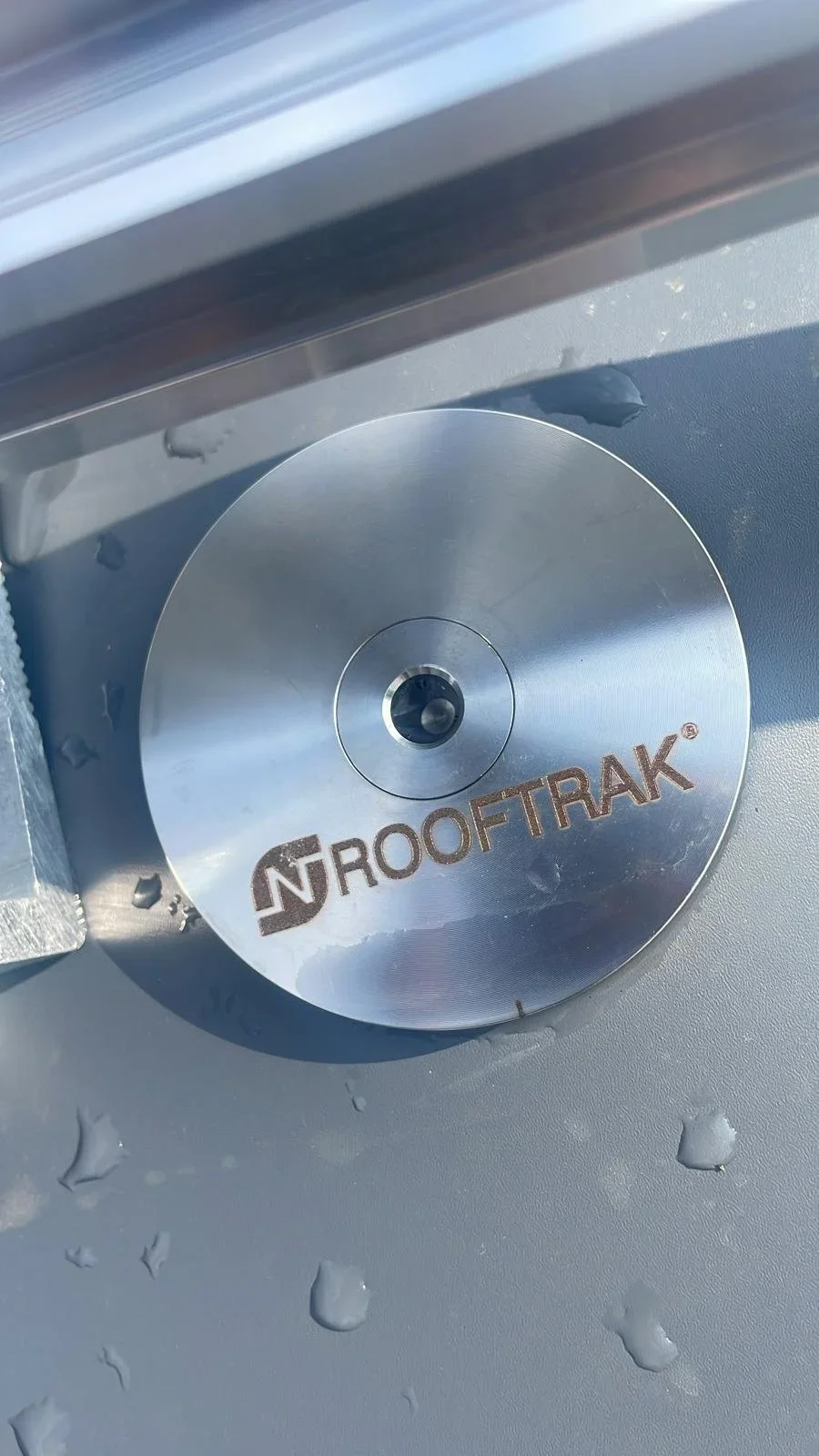 Close-up of a circular rooftop fixture labeled "NROOFTRAK" with water droplets on the surface.