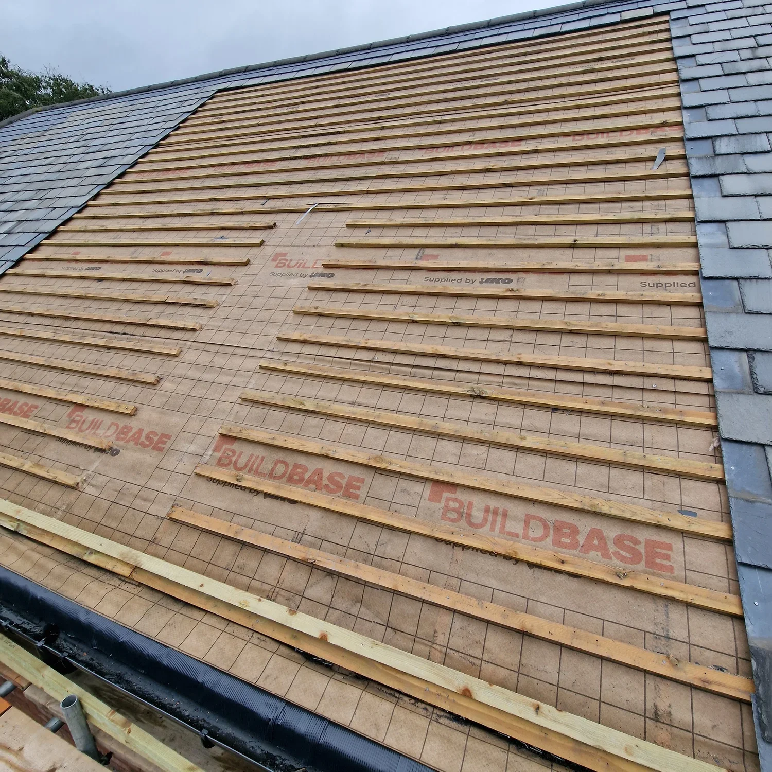 Roof construction with plywood sheets, wooden battens, and partial gray tile shingles on the sides.