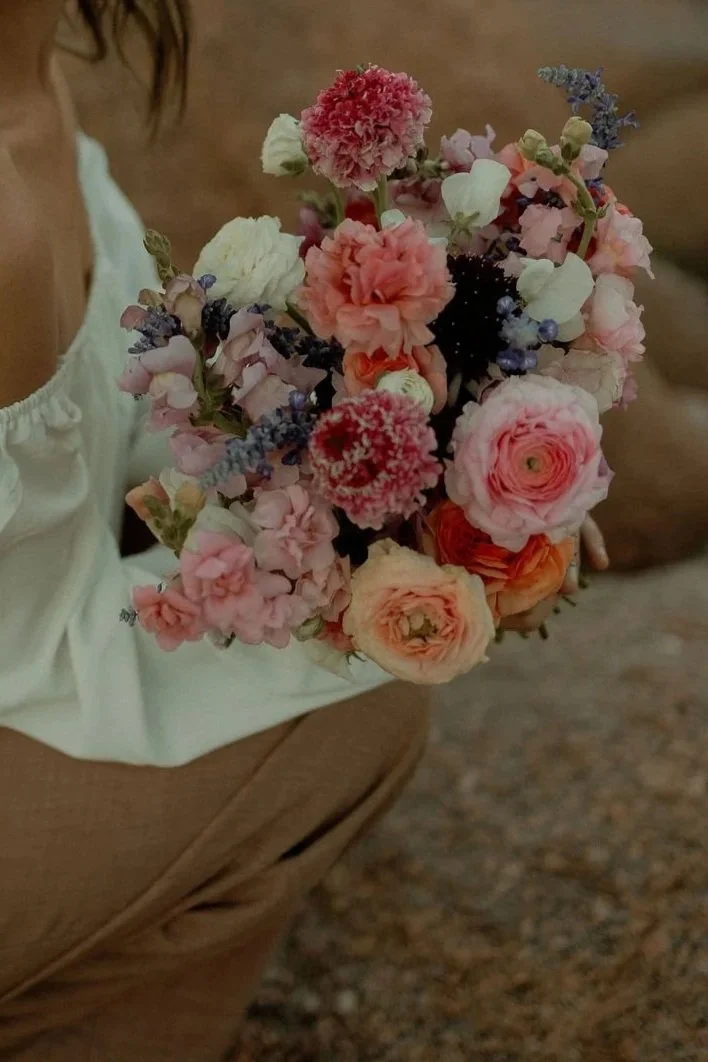 Person holding a colorful bouquet of pink, peach, purple, and white flowers.