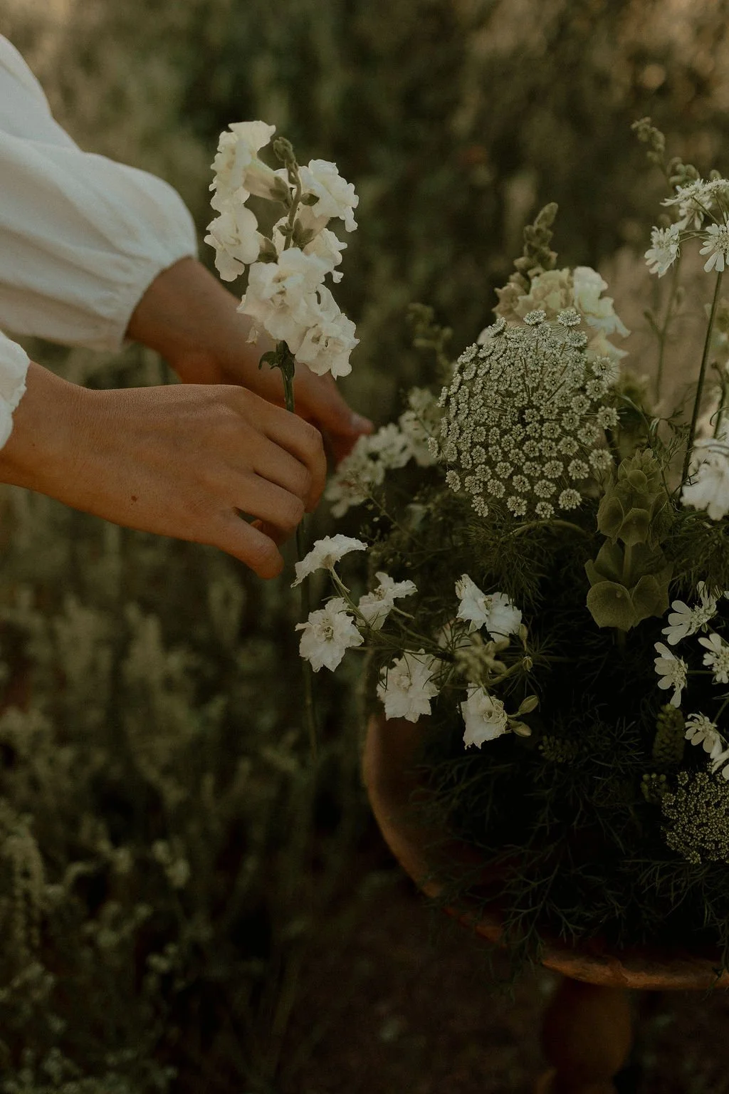 Person arranging white and green flowers in a basket