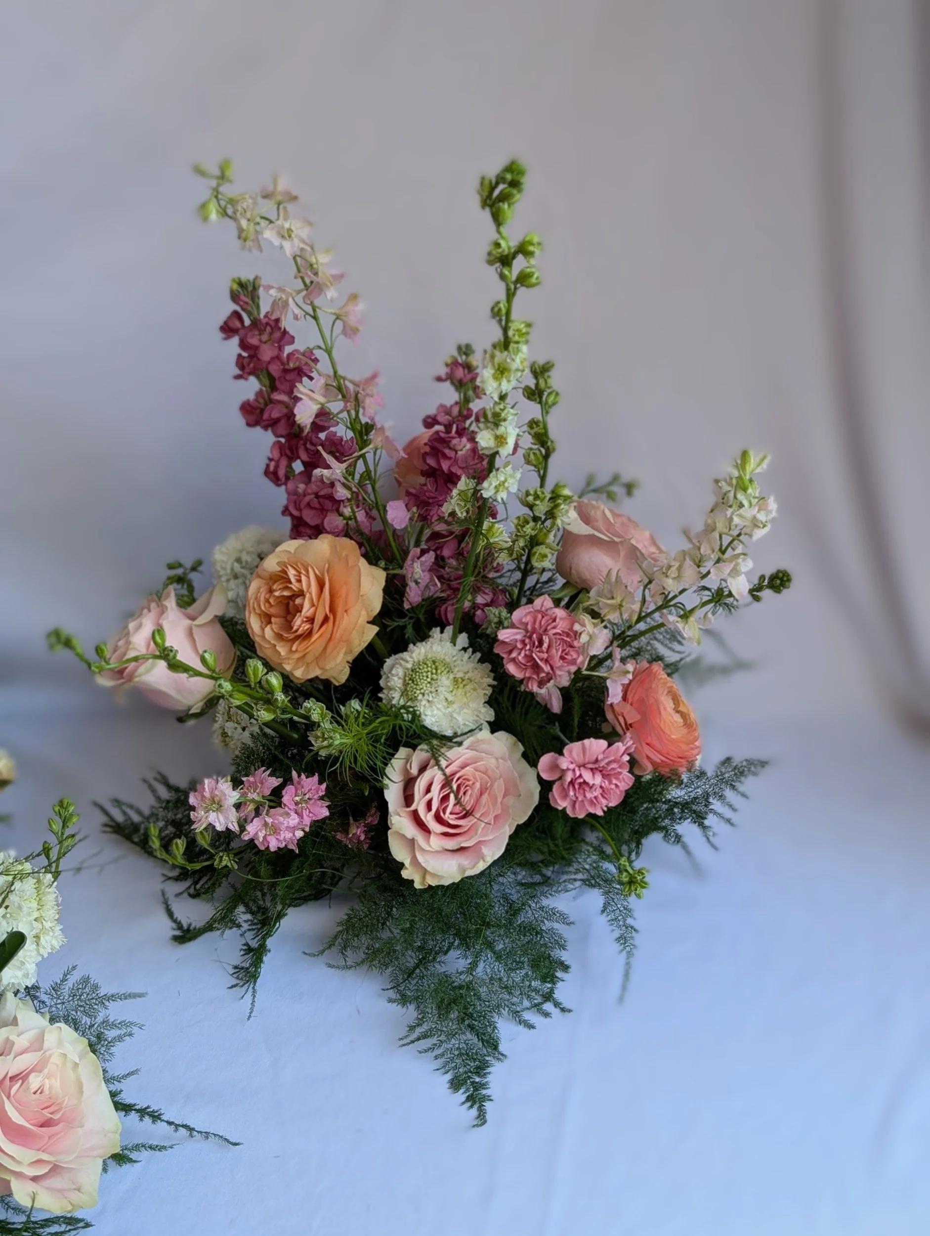 A floral arrangement with peach roses, pink carnations, white and pink snapdragons, and greenery on a white table