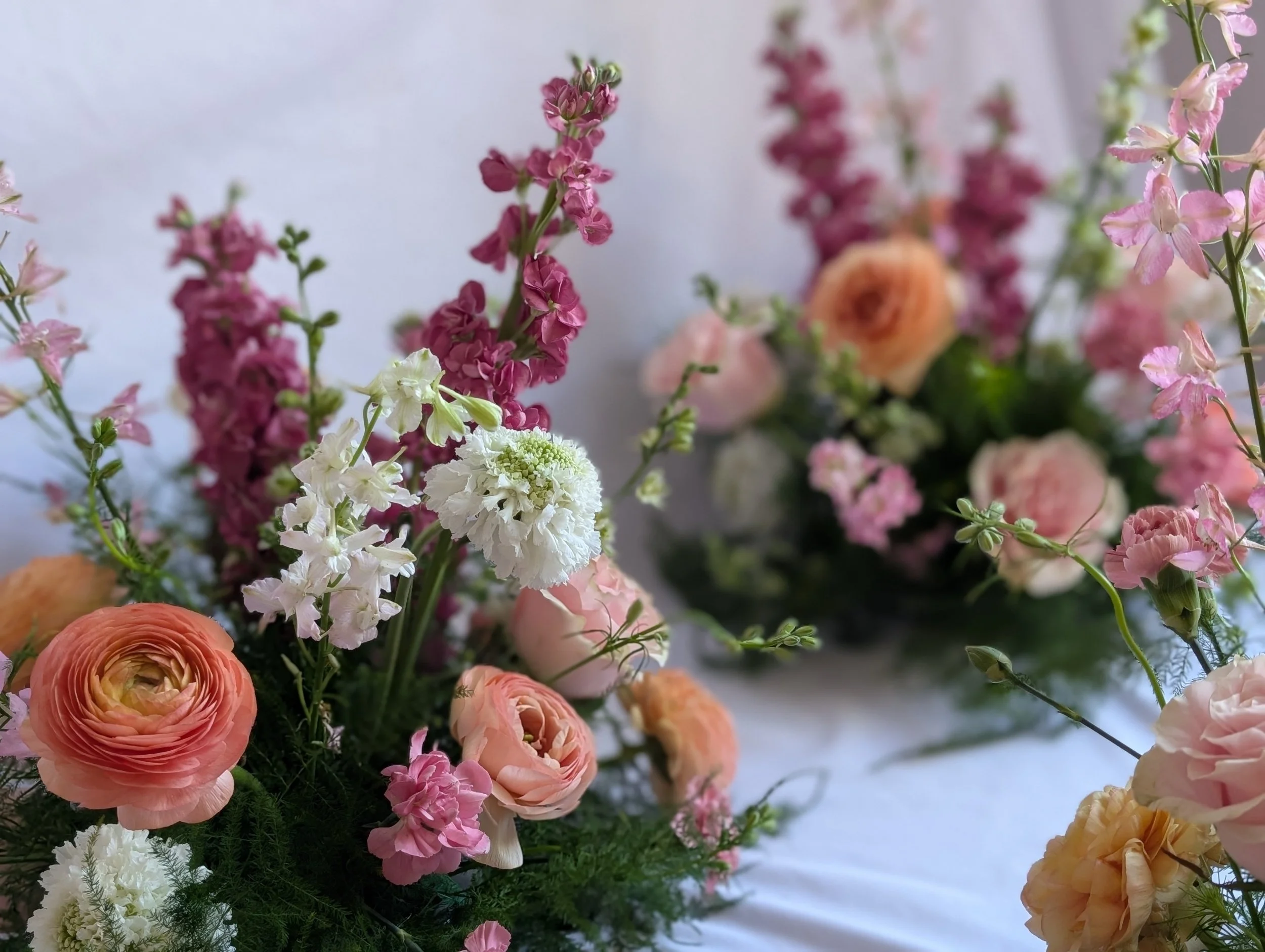 A bouquet of various pink, white, and peach flowers with greenery on a white background.