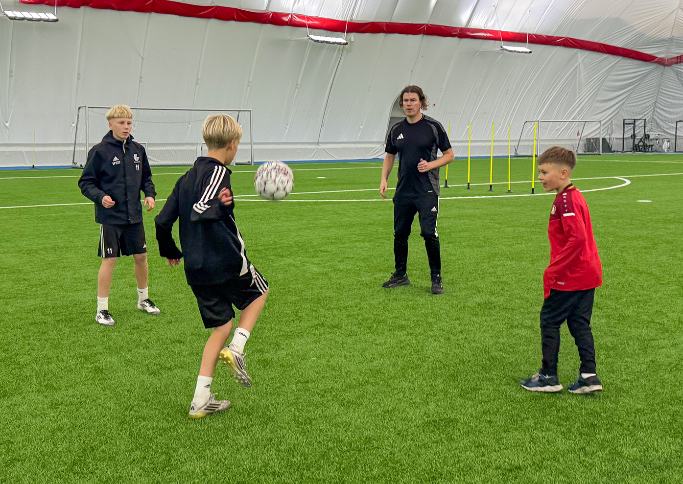 Lapsi ja aikuinen pelaavat jalkapalloa harjoituskentällä sisätiloissa.