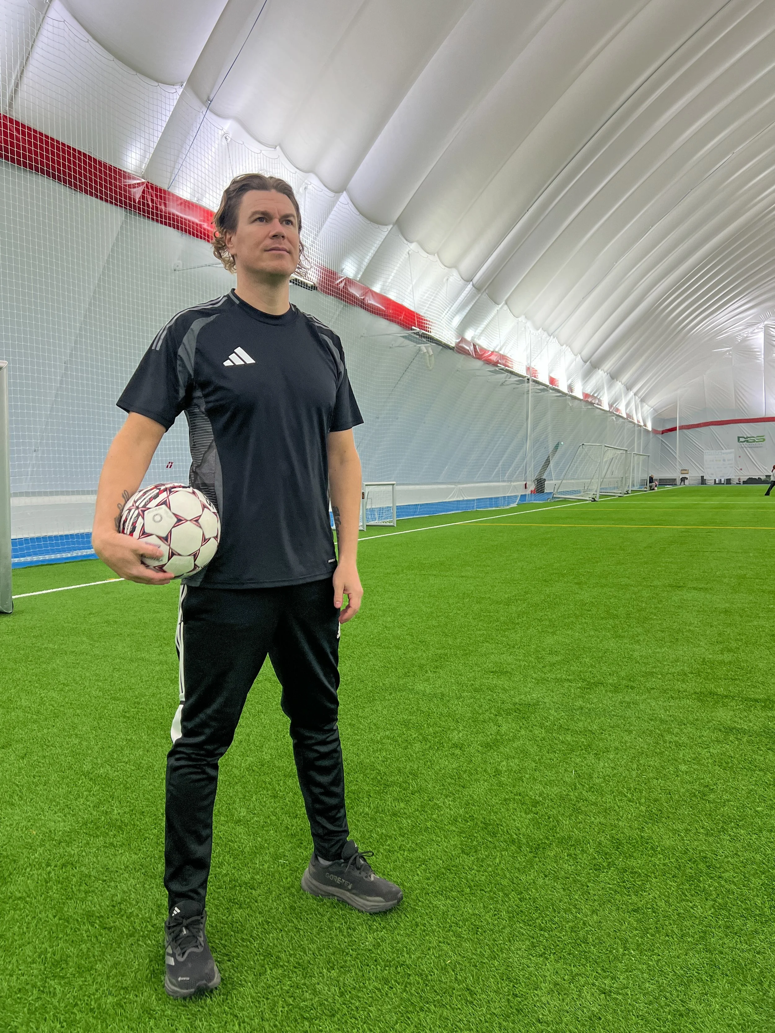 Mies hockeyjoukkueen varusteissa treenihallissa, kädessään jalkapallo.