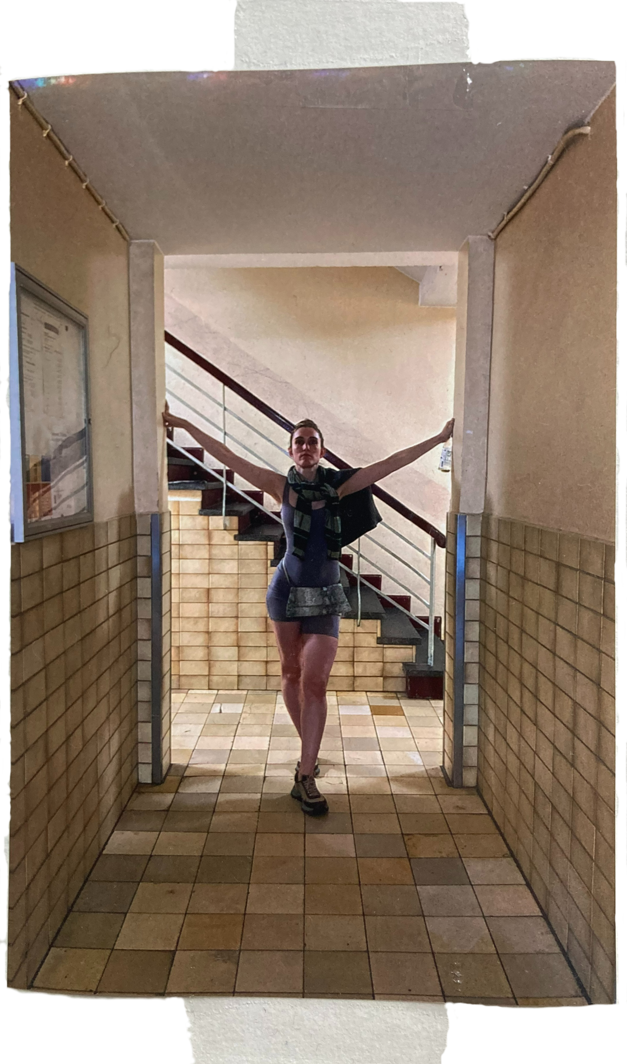 Frau in Sportkleidung mit offener, selbstbewusster Körperhaltung vor Treppe in einem Hausflur.