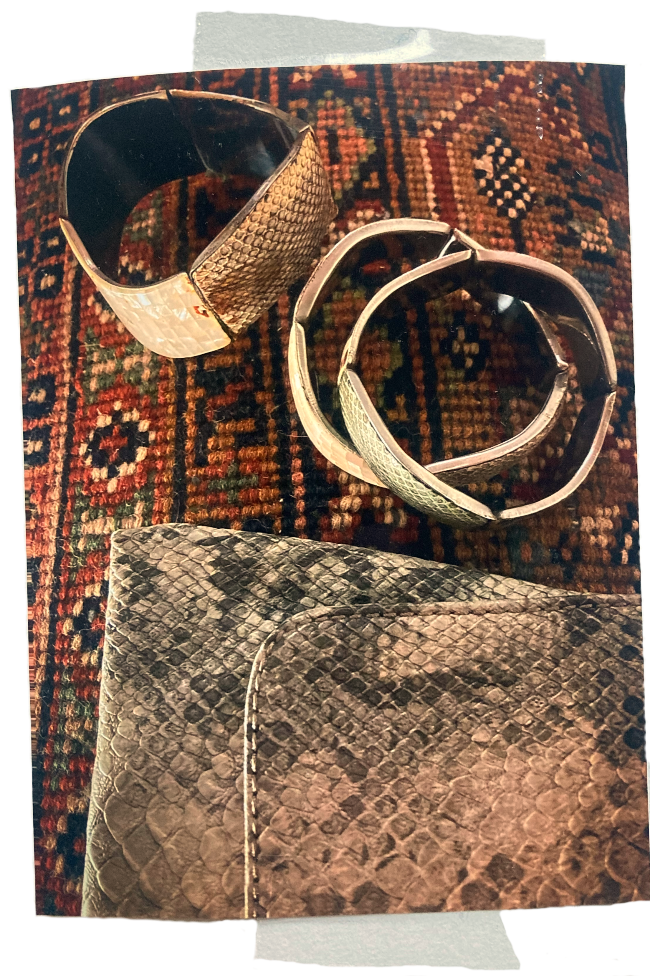 Armbänder im Schlangenleder-Design als modische Accessoires, arrangiert auf buntem Teppich mit passender Clutch.