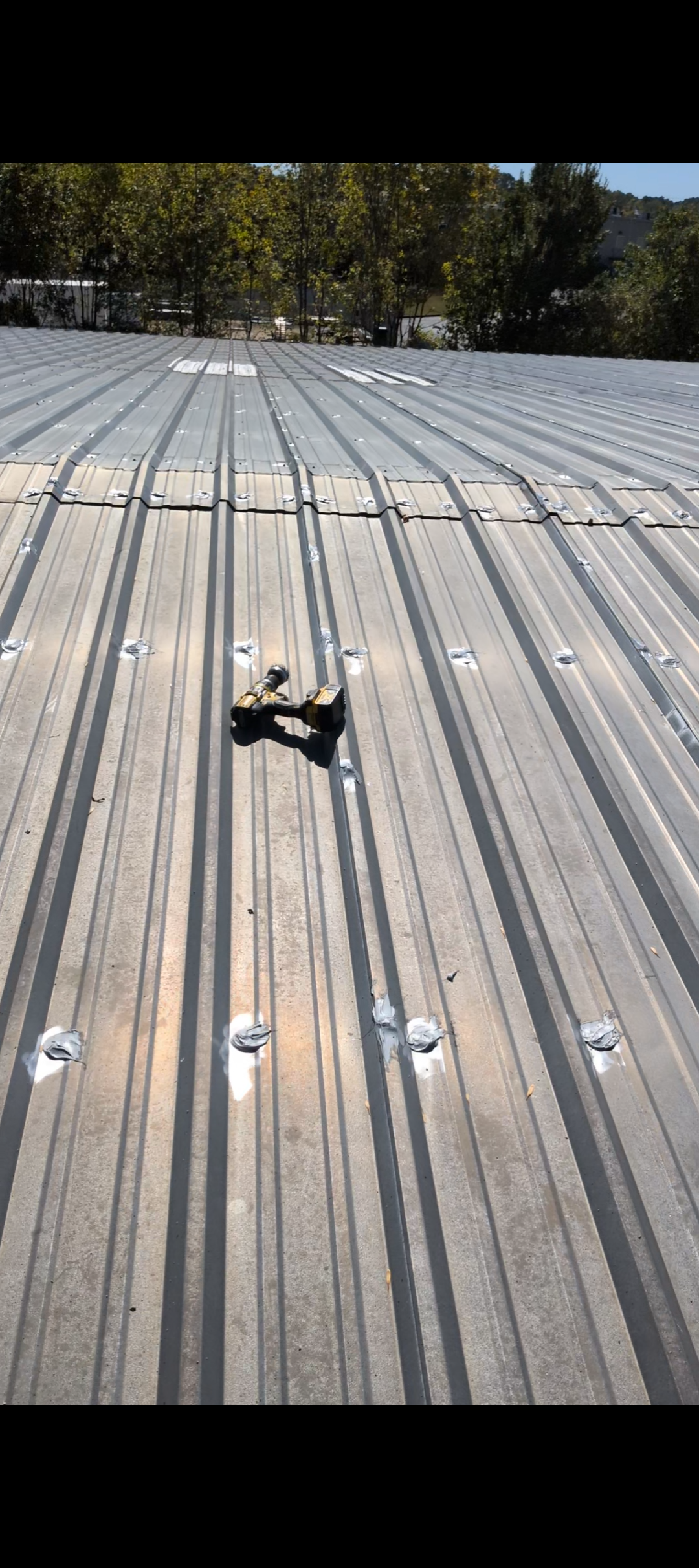 A metal roof under construction with a cordless drill lying on it and visible fasteners and sealants.