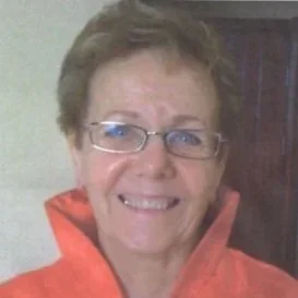 A smiling woman with short hair and glasses, wearing an orange jacket.