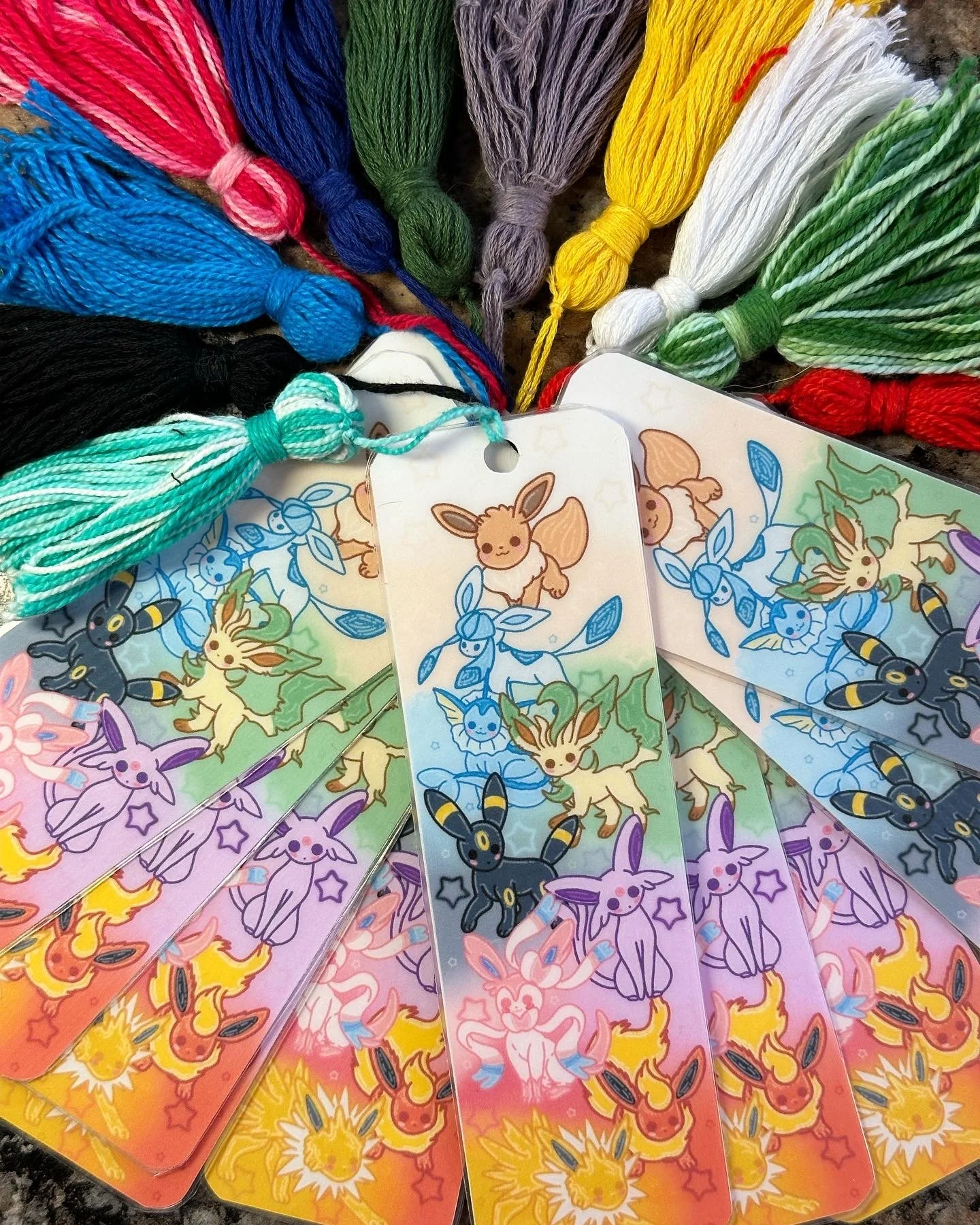 Colorful embroidered tags with Pokémon-themed designs featuring Eevee, Sylveon, Umbreon, Espeon, and Jolteon. Several skeins of multicolored embroidery floss are also visible.