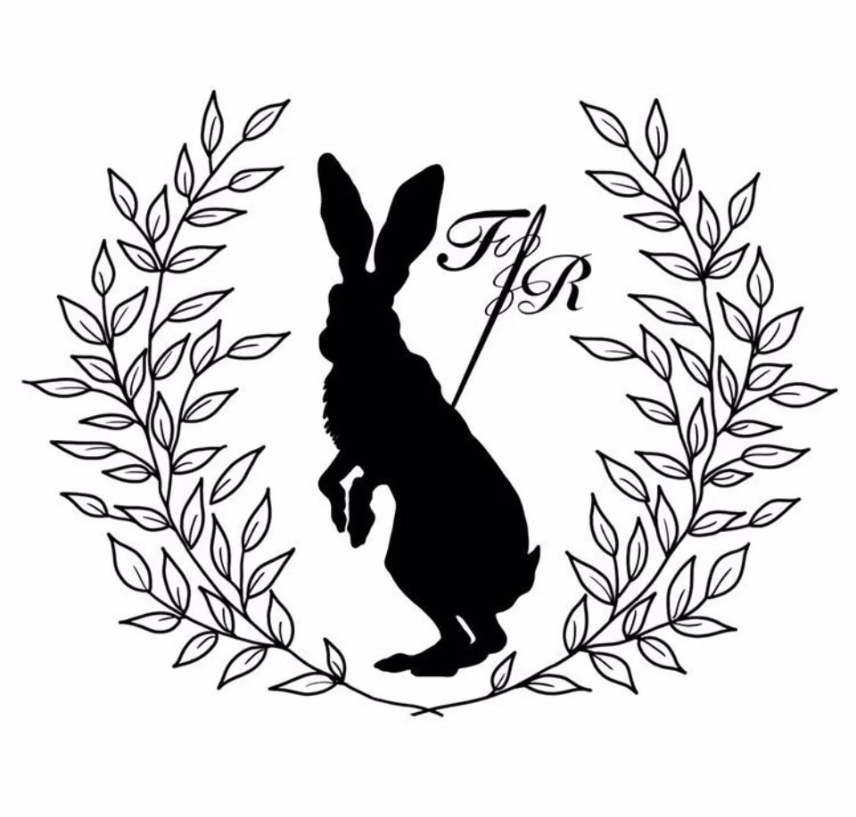A silhouette of a rabbit holding a flag, surrounded by a laurel wreath, with the initials ‘F  R' written in elegant script.