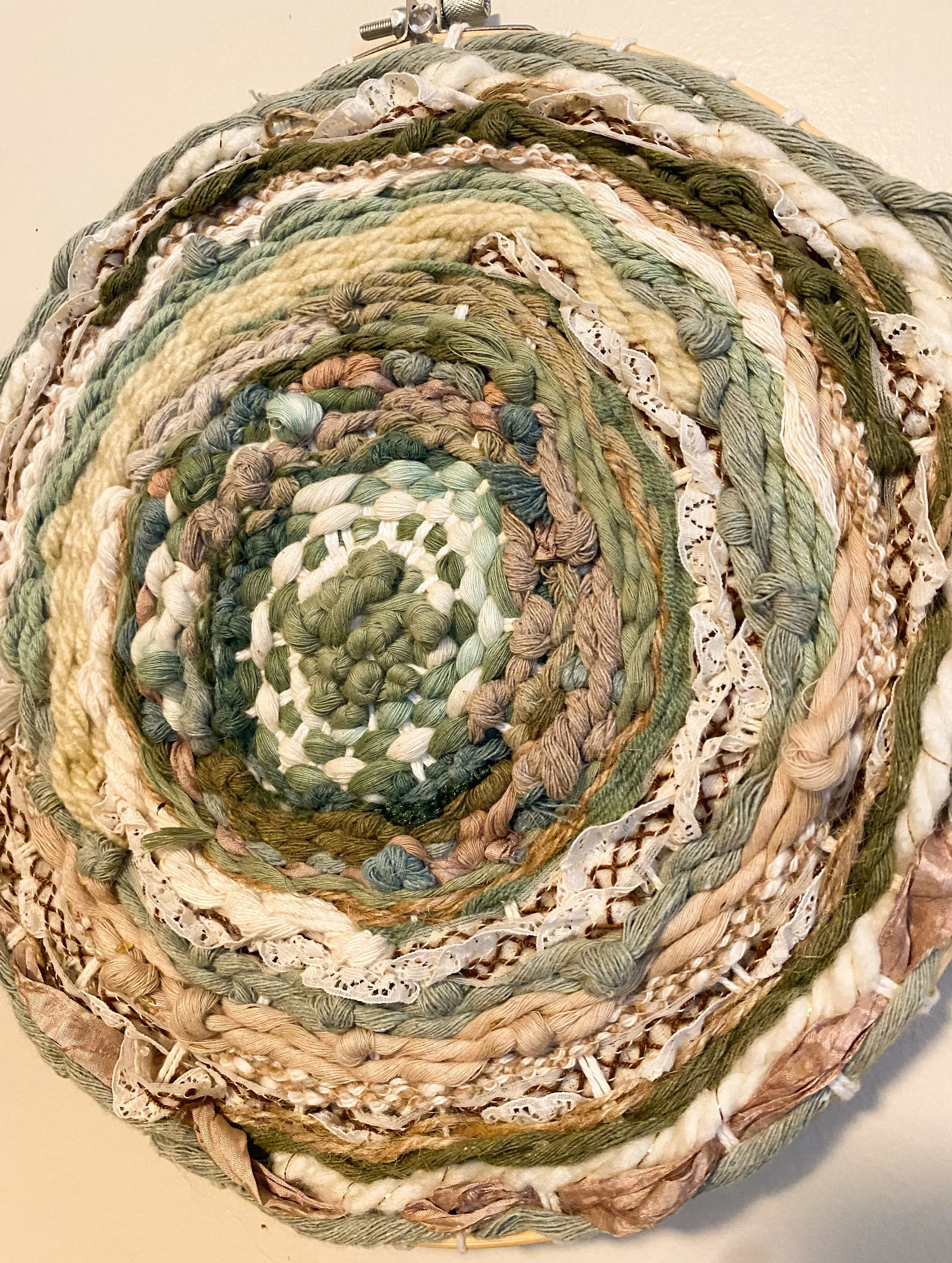 Coiled arrangement of variously colored fabric strips, including green, beige, and white, on a circular base with a metal clip at the top.