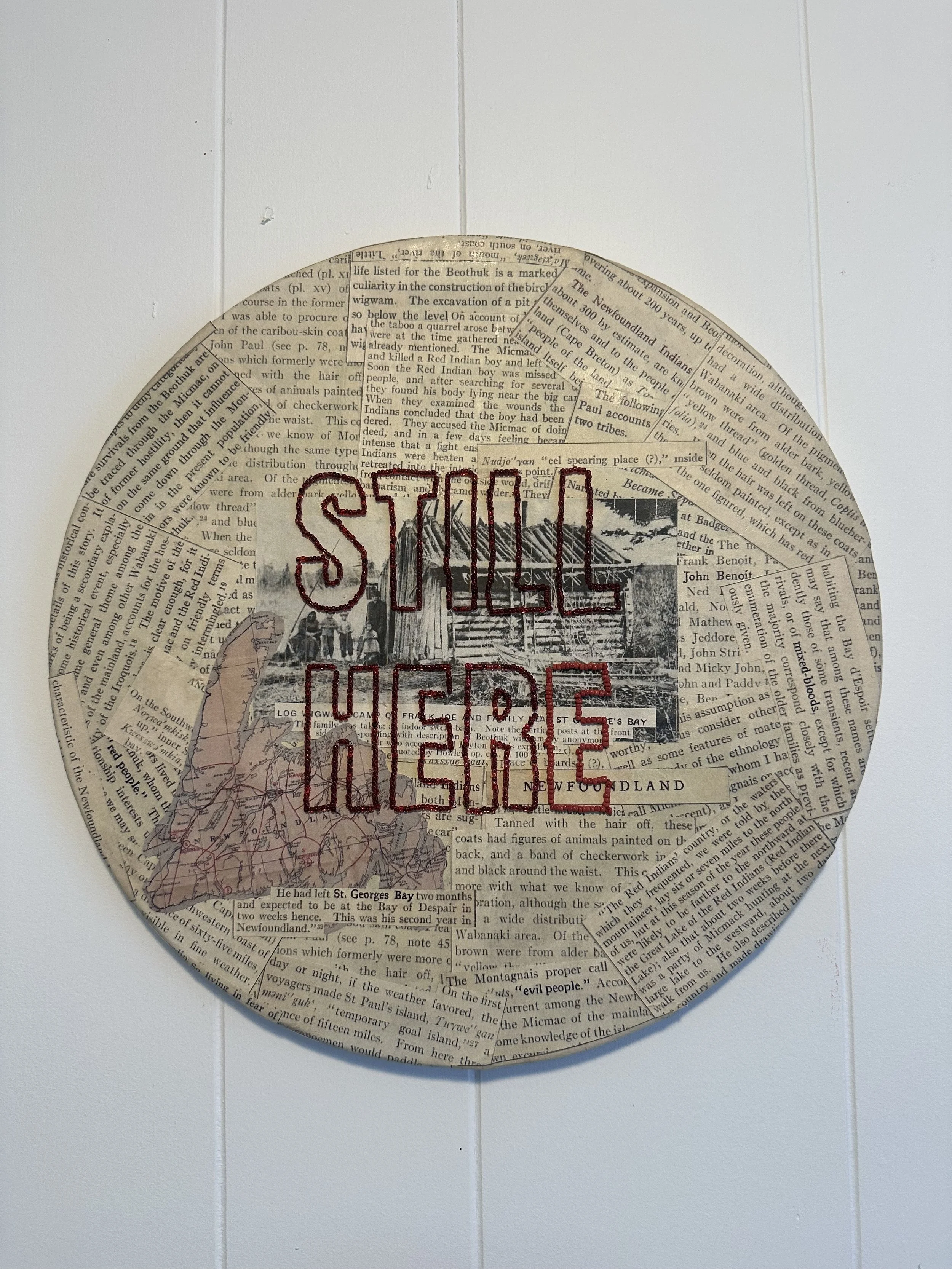 A circular collage art piece made from cut-out newspaper clippings, with a black and white image of a mi’kmaq settlement in Newfoundland, Canada. Overlaid with red embroidered text that reads ’STILL HERE'.