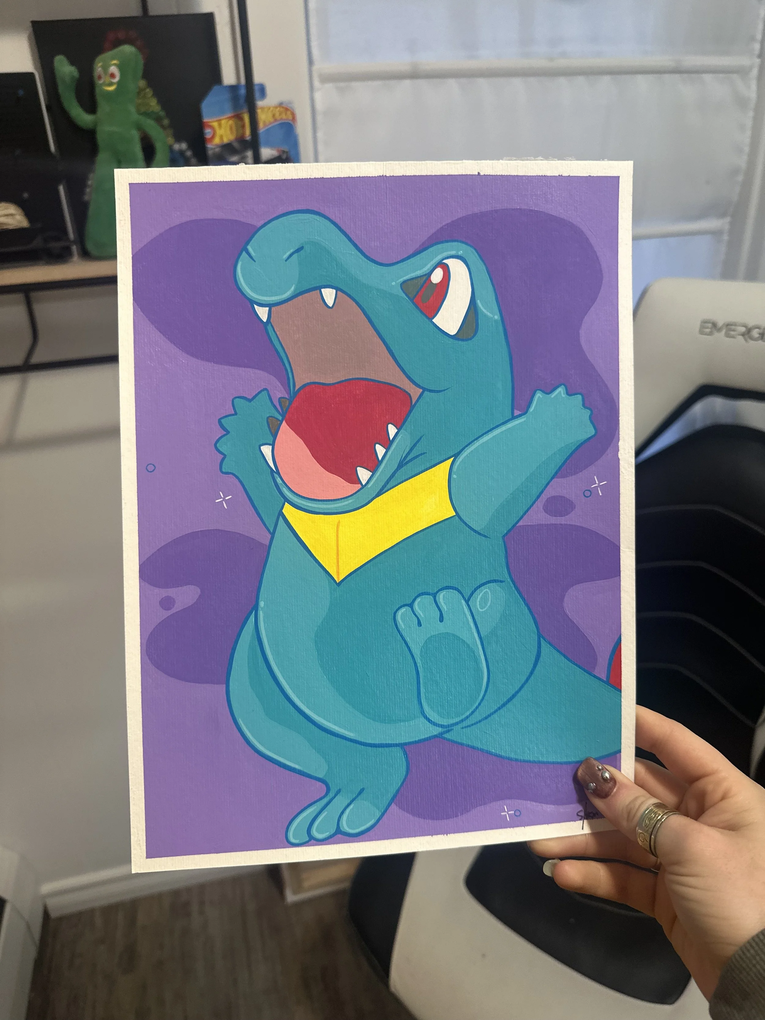 A colorful cartoon illustration of a crocodile wearing a yellow superhero cape, with an open mouth showing teeth, set against a purple background.