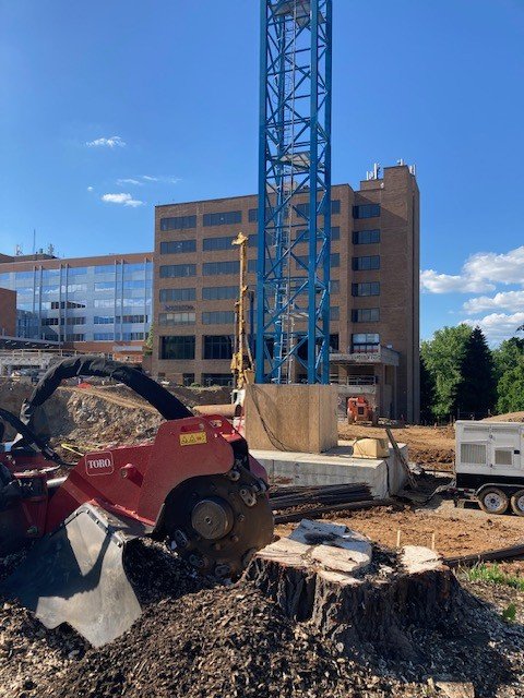 Construction site with a blue tower crane, a building in the background, and a red construction saw in the foreground.