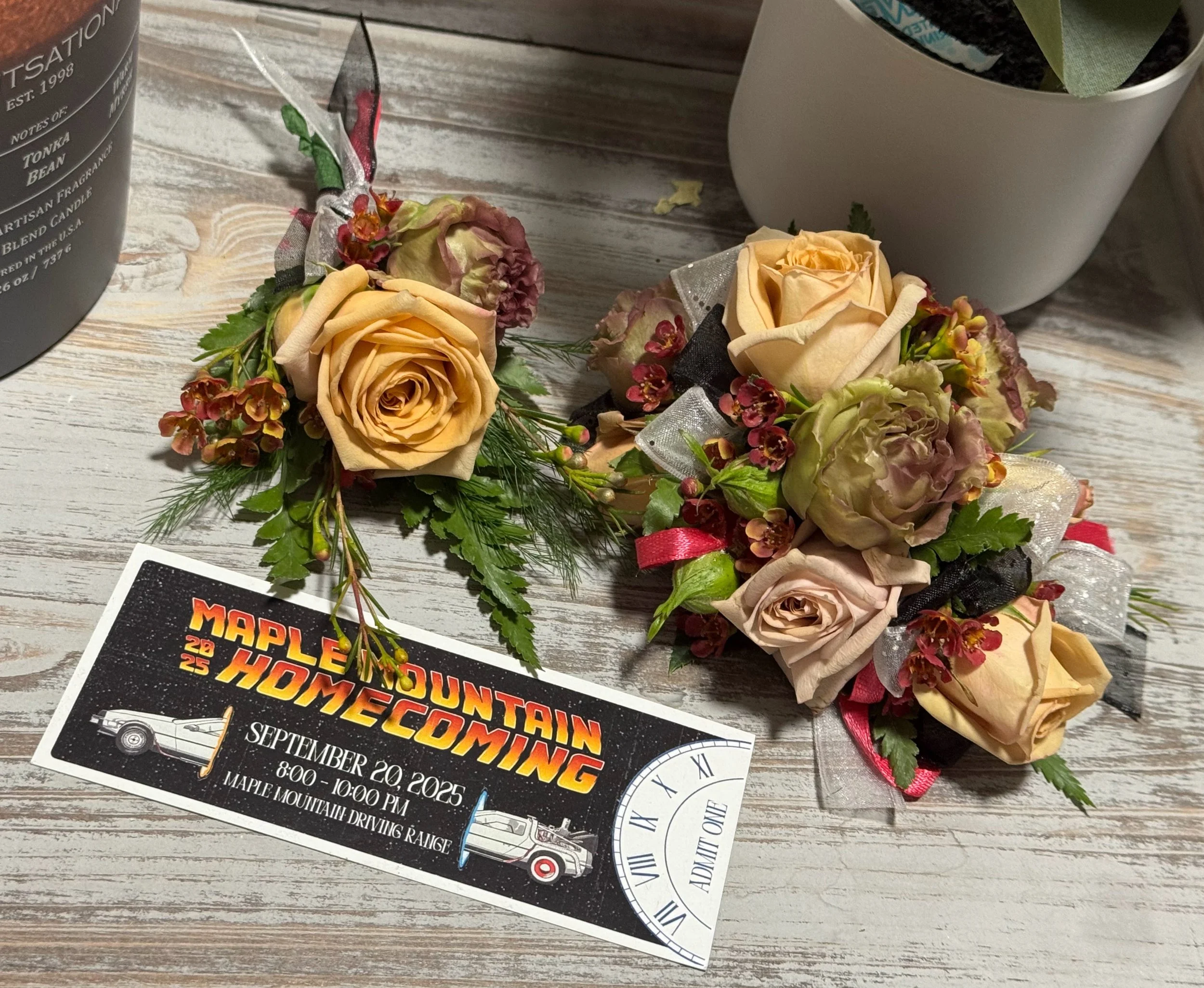 Wedding boutonniere and corsage decorated with peach and beige roses, small red flowers, greenery, and ribbons, placed near a homecoming event ticket for Maple Mountain Homecoming on September 20, 2025, at Maple Mountain Driving Range.