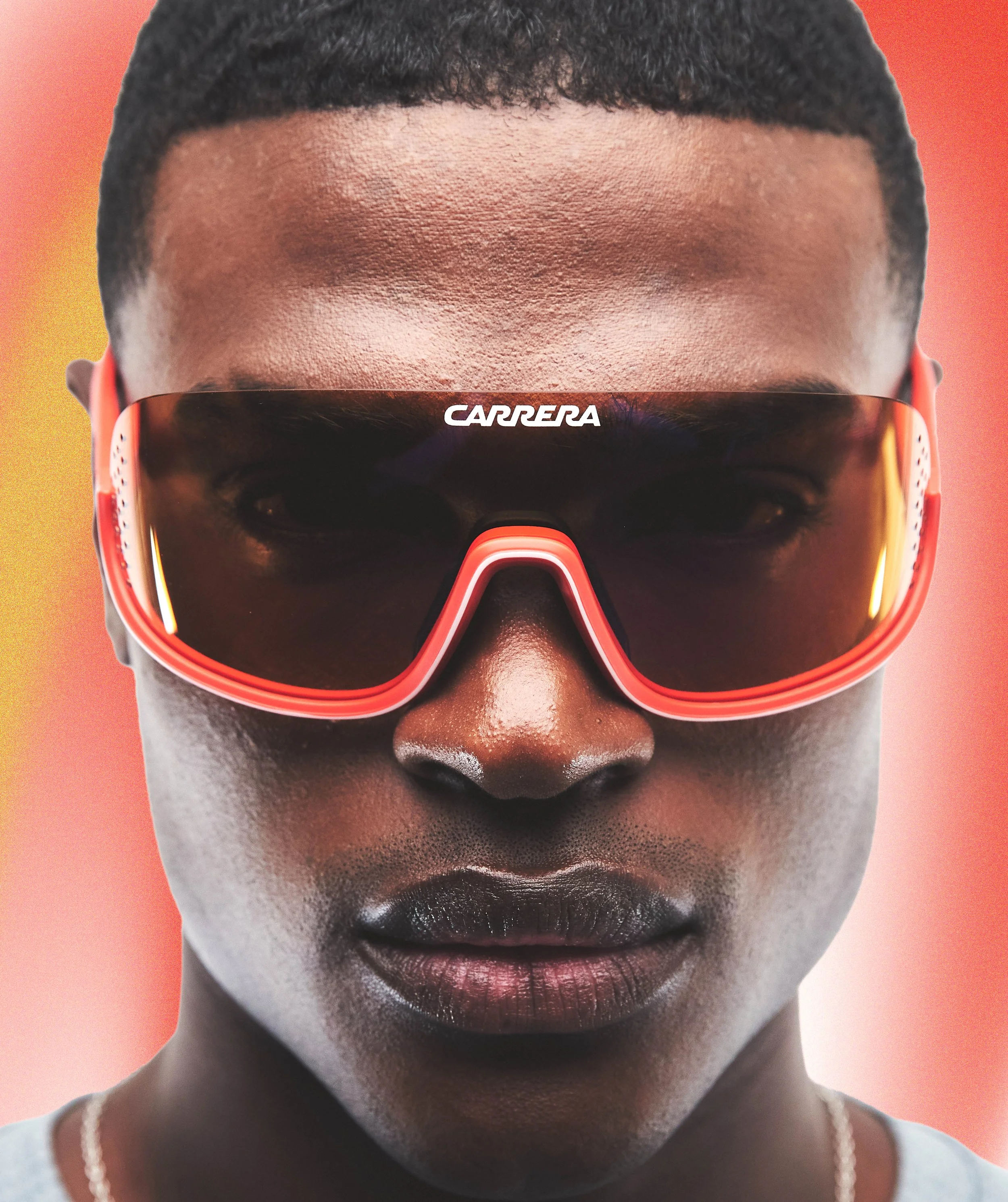 Close-up of a person's face wearing red sunglasses with the word 'CARRERA' on the front, with a blurred background.