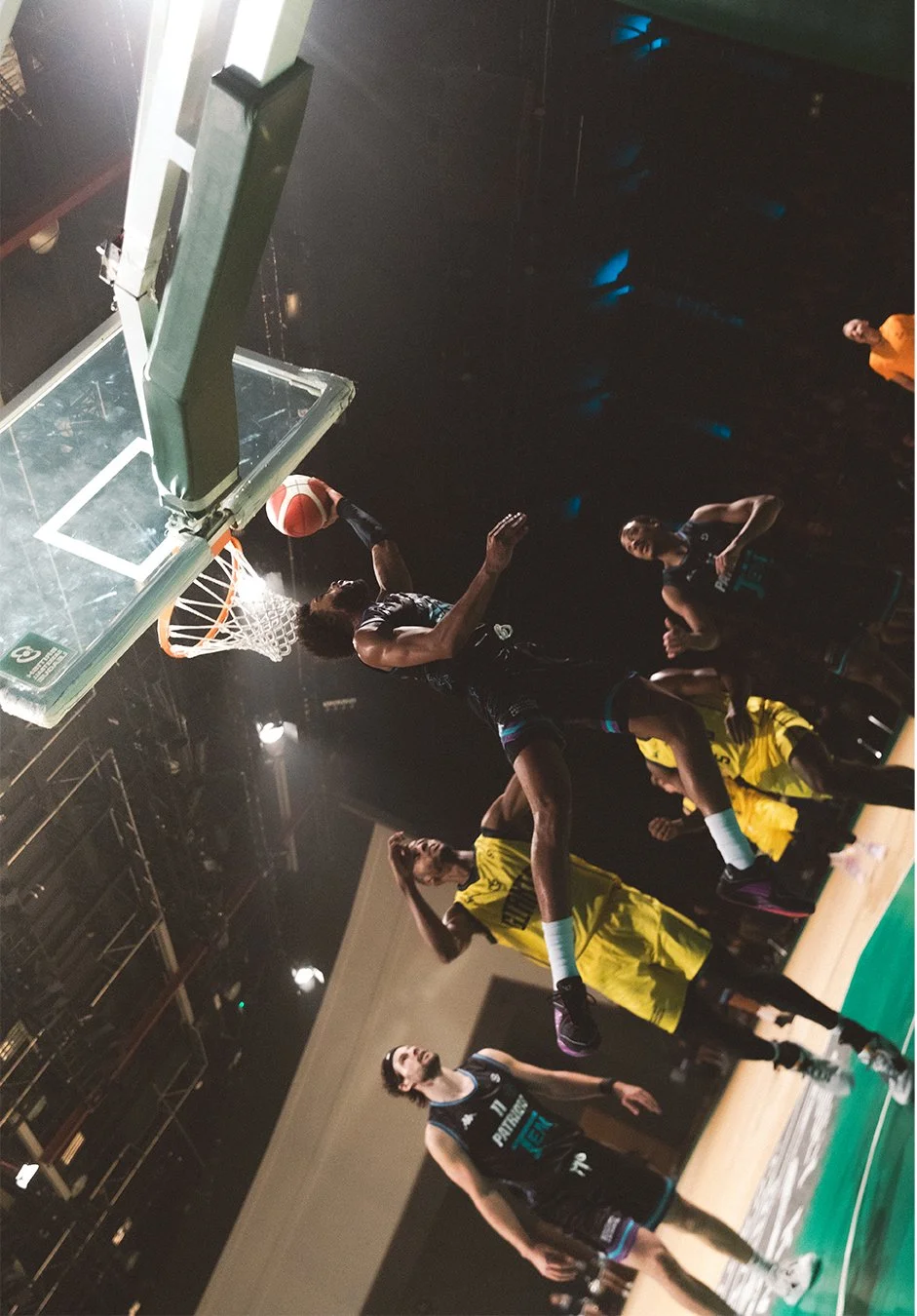 Basketball game with players in action, one player jumping to shoot or dunk, others watching on the court.