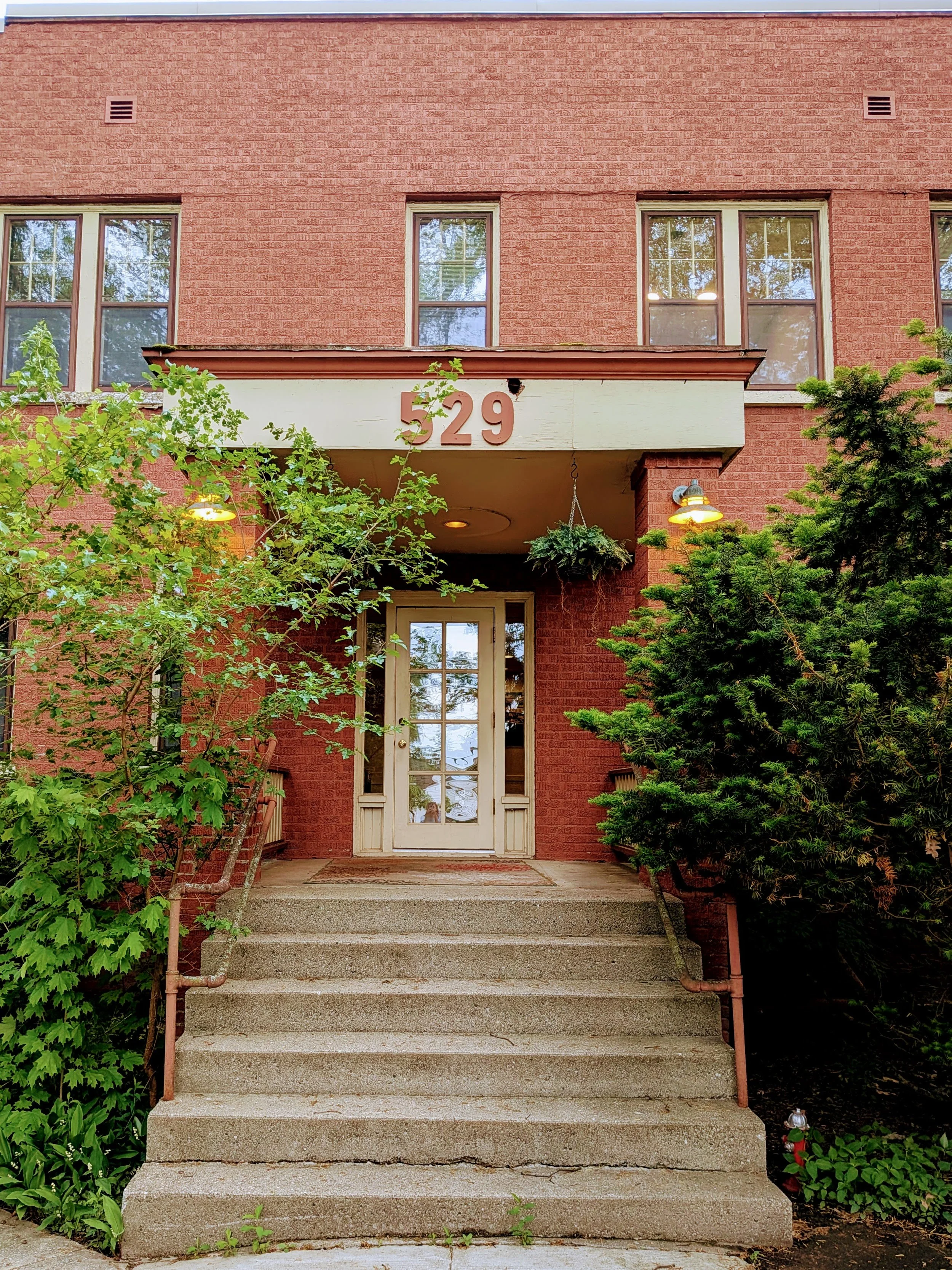 Entrance to brick building with number 529 displayed above door and concrete steps leading to glass paneled door and green bushes on either side. In-person Christian Counseling with Irene Kraegel, PsyD, in Grand Rapids and online through PsyPact.