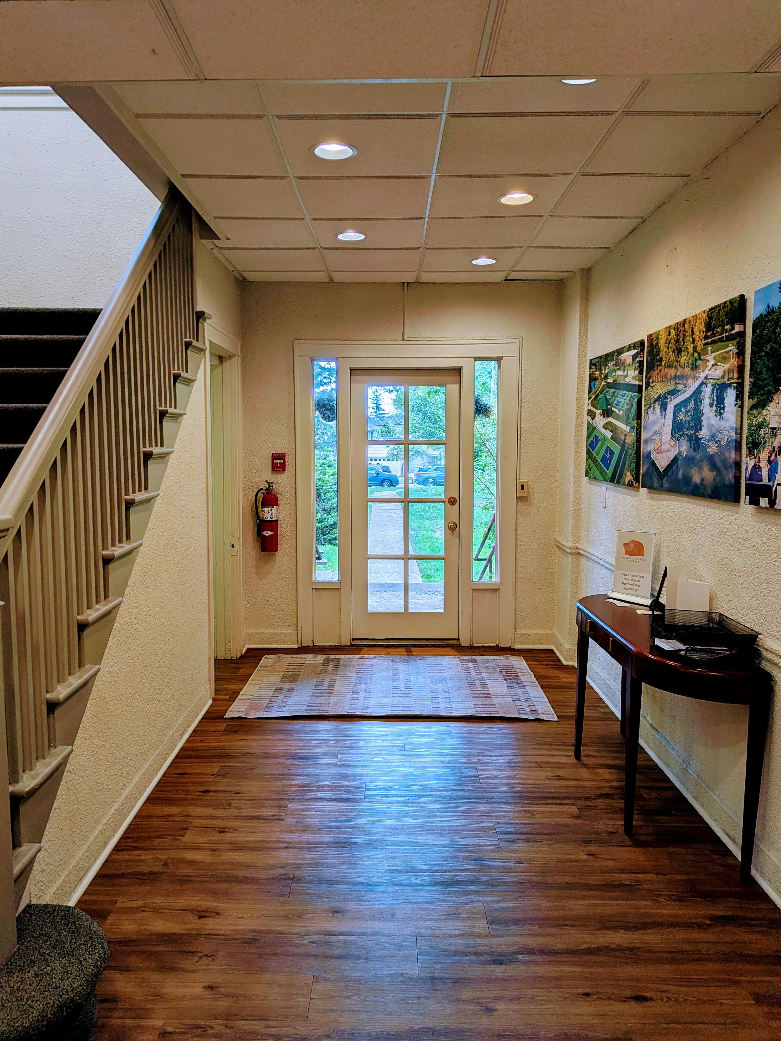 Interior view of building lobby with glass door entrance, wooden flooring, a small rug, a side table, and wall paintings. Irene Kraegel, PsyD provides in-person (Michigan) and virtual Christian counseling for anxiety, depression, and chronic pain.