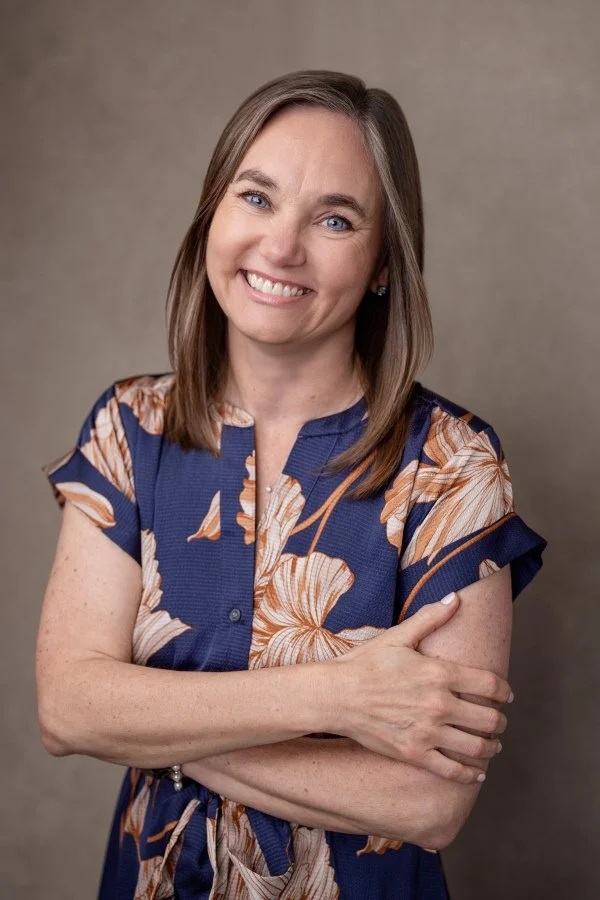 Dr. Irene Kraegel smiles with blue eyes, light brown hair, relaxed with arms cross, wearing blue dress with brown & tan flowers. Anxiety/depression, chronic pain, & faith-based therapy available in Grand Rapids, MI & online in 43 PsyPact states.