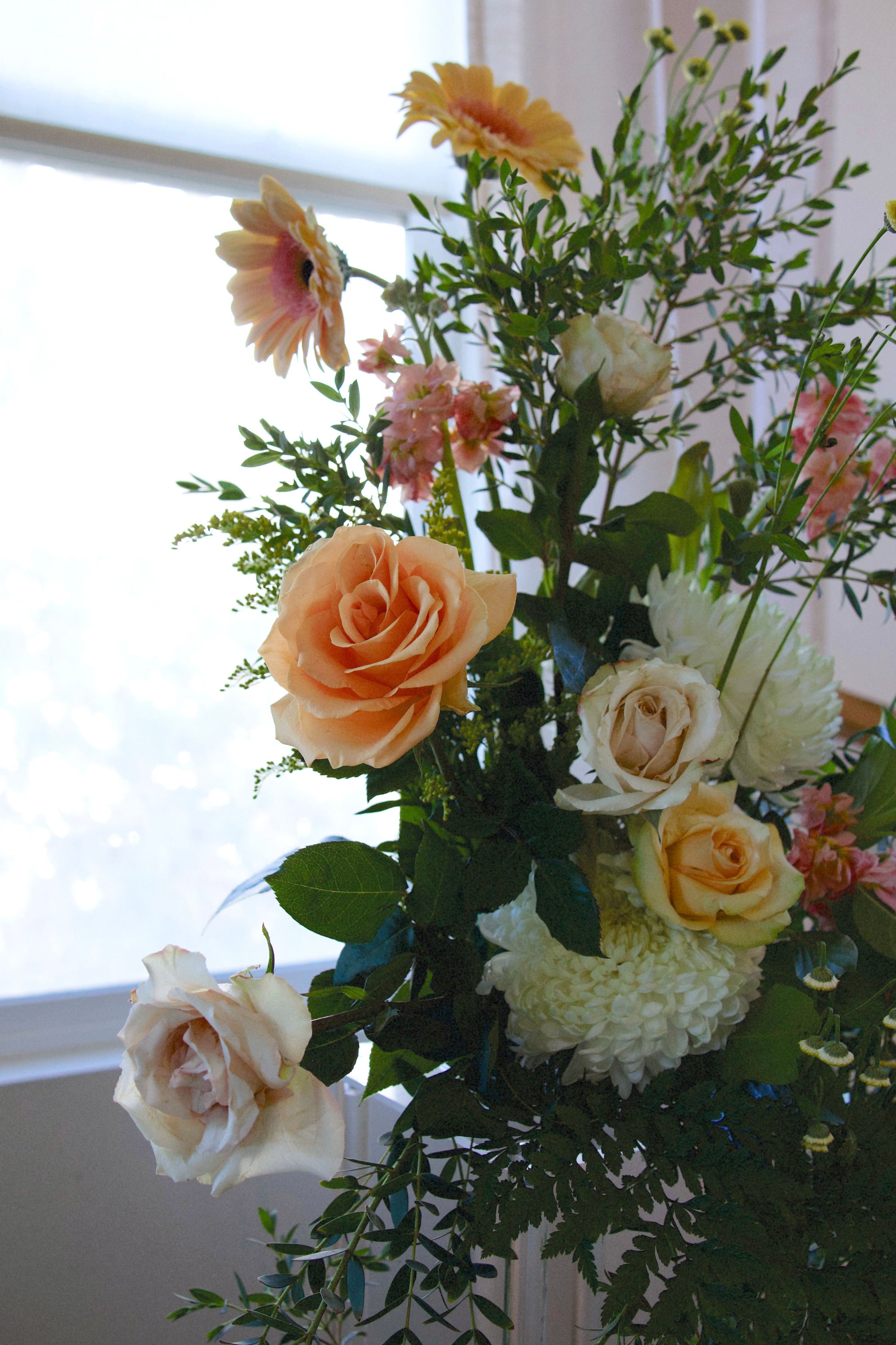 A bouquet of fresh flowers including roses, daisies, and other blooms arranged indoors near a window.