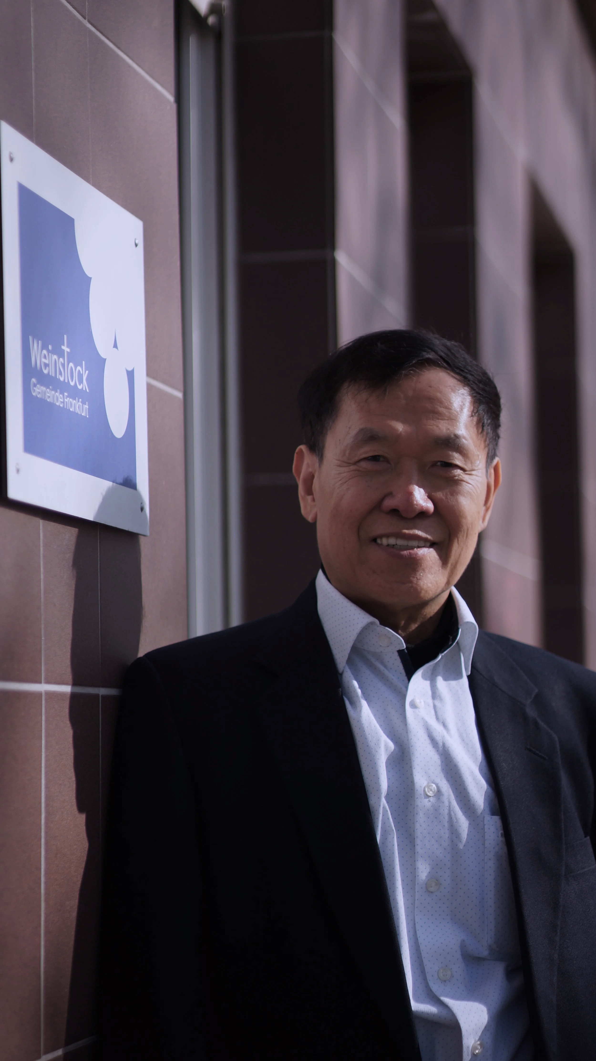 Abraham Park, a pastor in the church, is standing next to a wall with a sign that reads "Weinstock, Gemeinde Frankfurt."