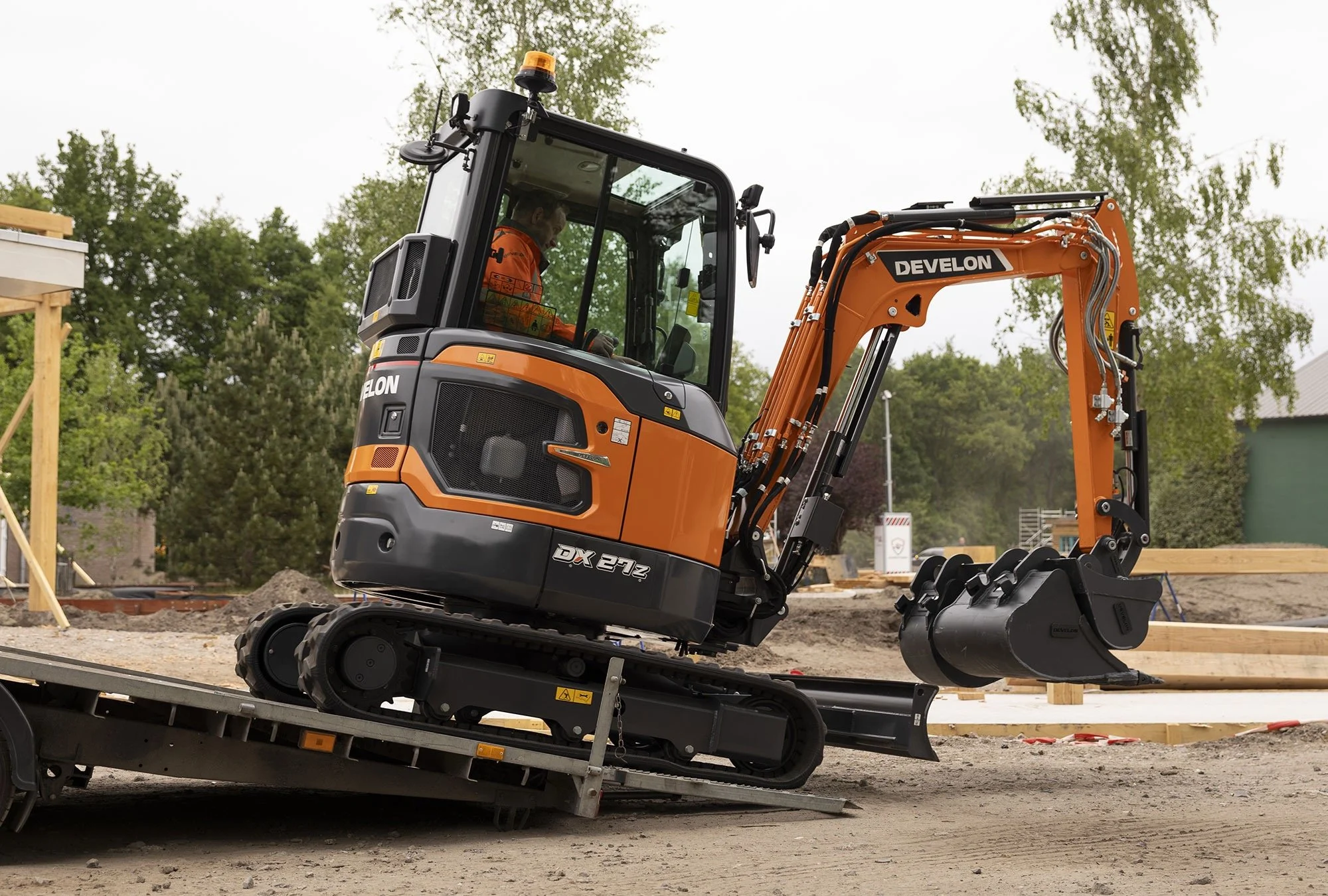 A small orange and black excavator on a construction site, with a person operating it inside the cab.