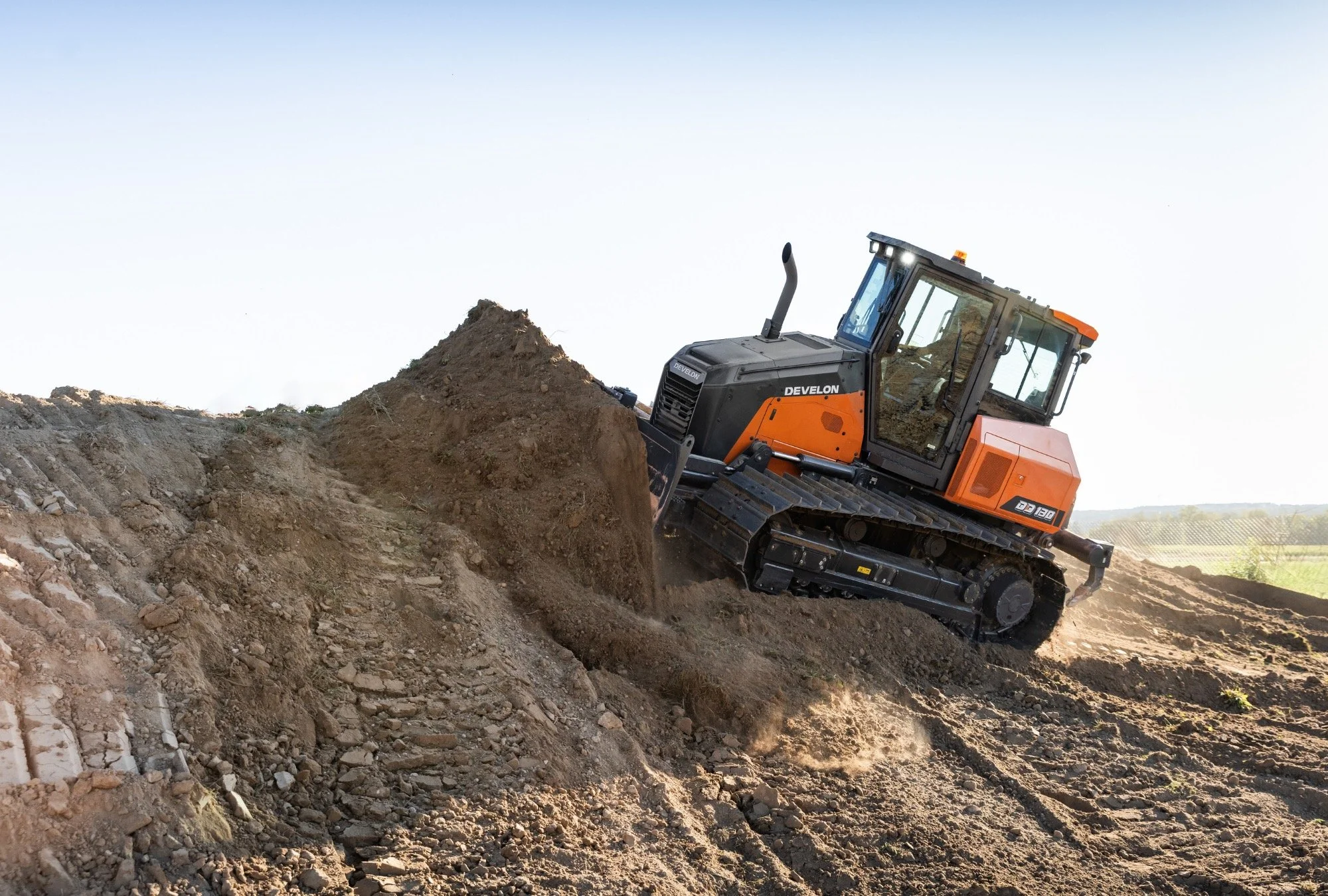 A black and orange bulldozer moving dirt on a construction site with a clear sky in the background.