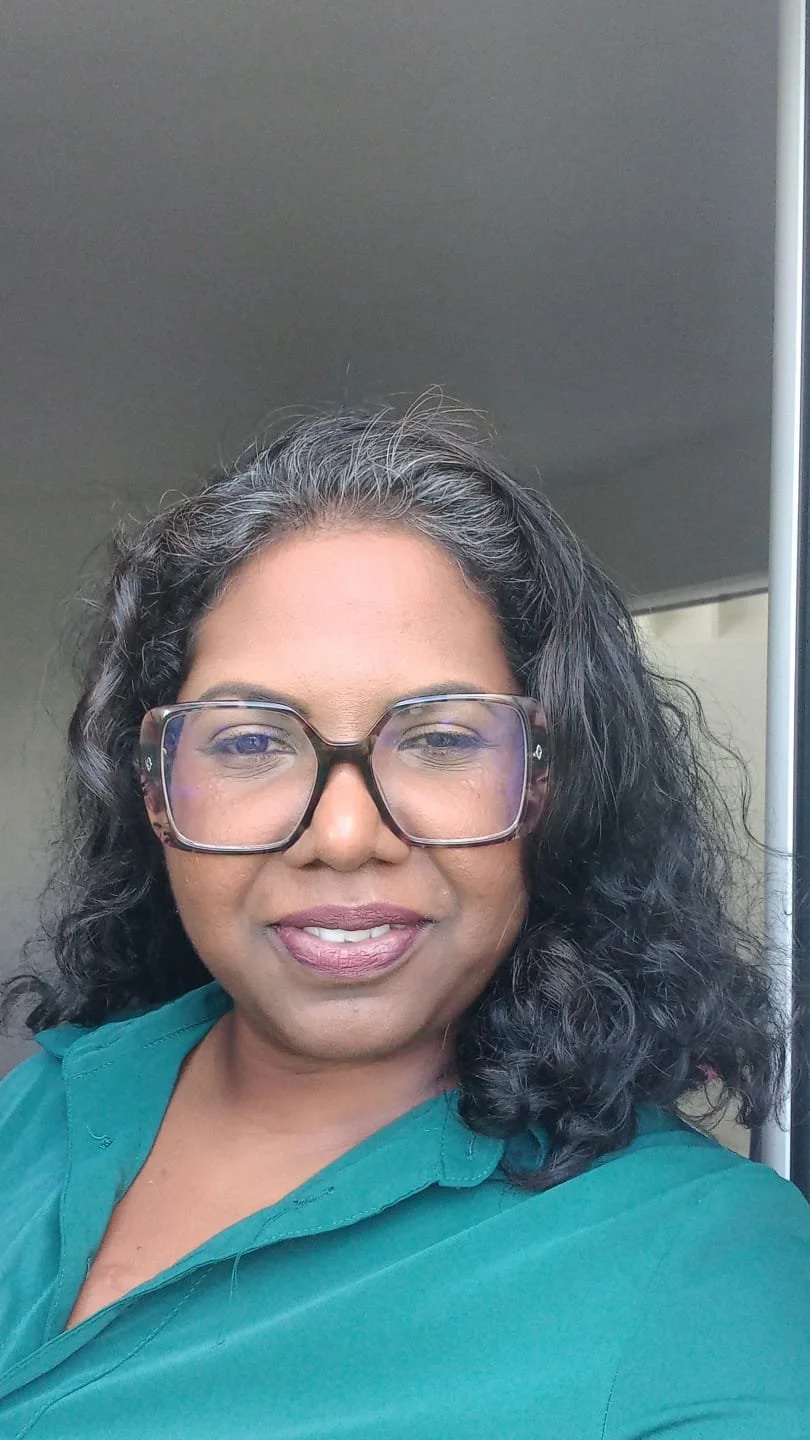 Une femme à lunettes, avec des cheveux ondulés, portant une chemise verte.